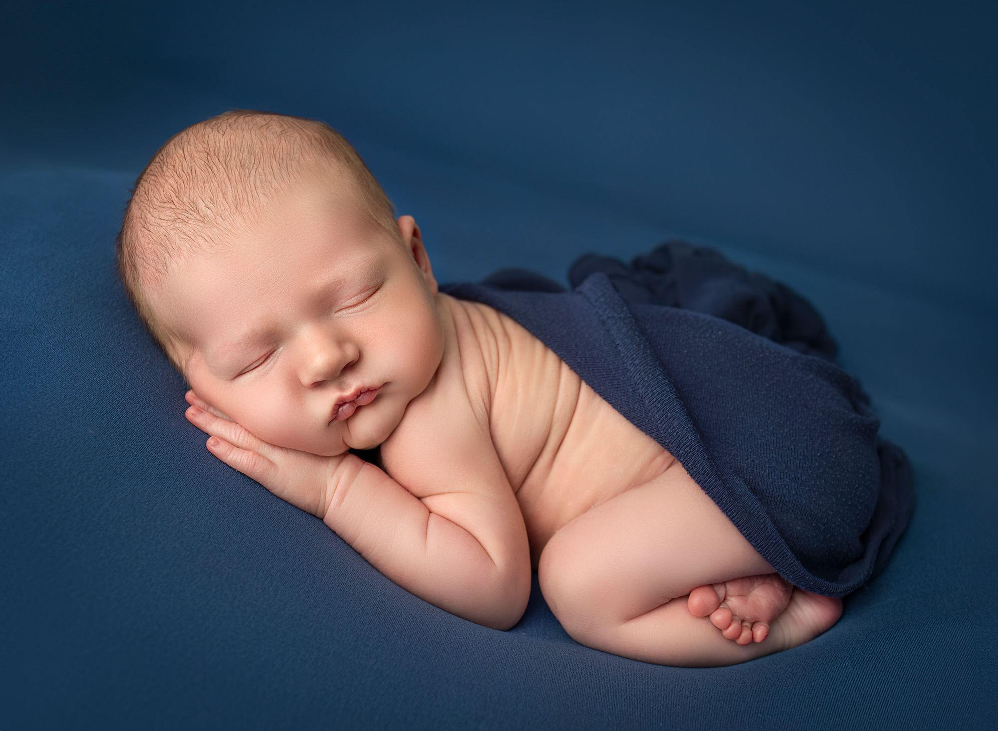 Baby Owen's back wrinkles against a dark blue wrap