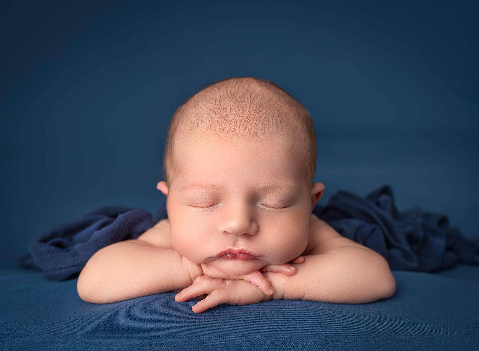 Baby Owen resting his head on his hands on a navy blue background