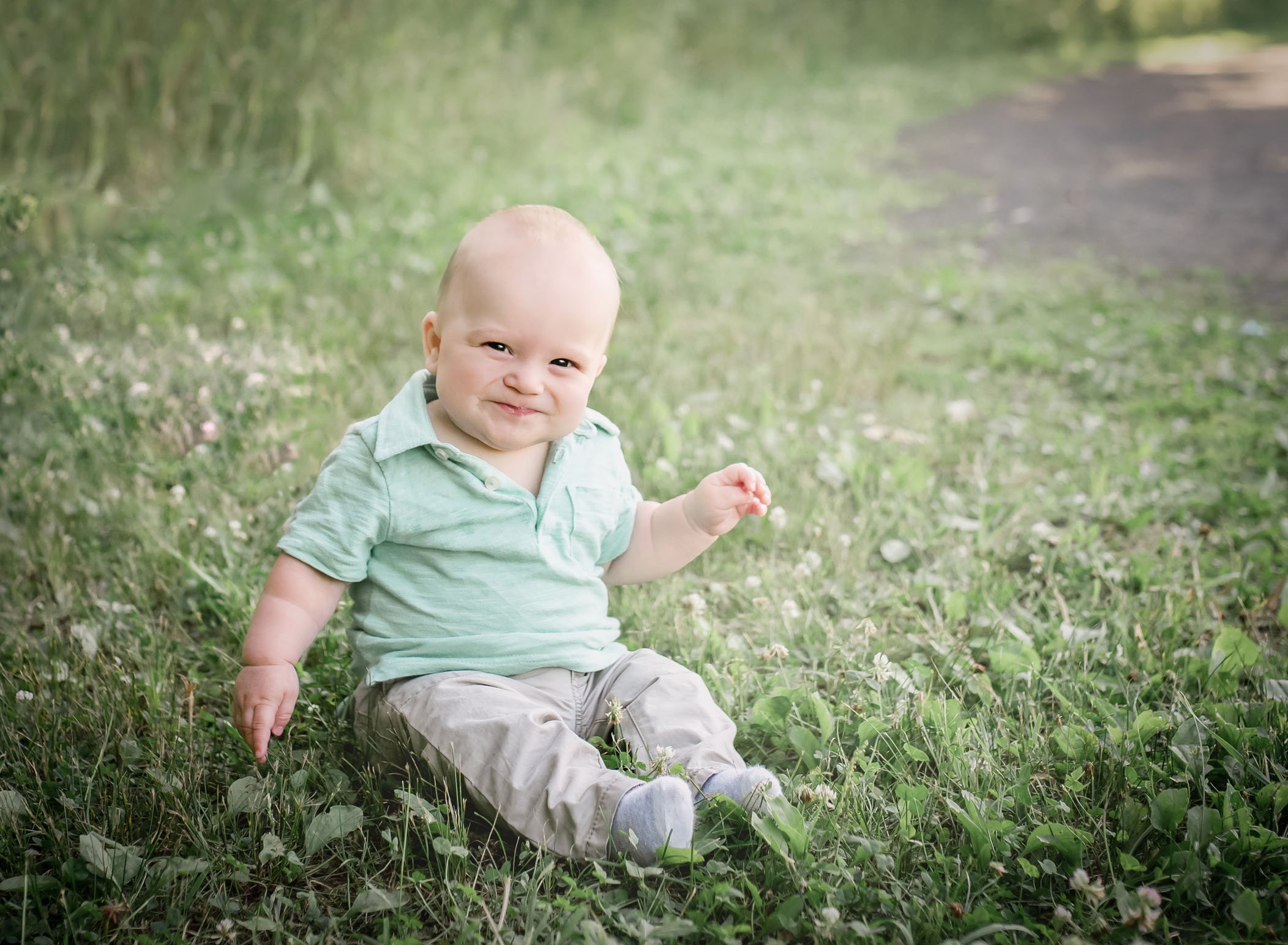 6 month old baby boy sitting up in the grass grinning