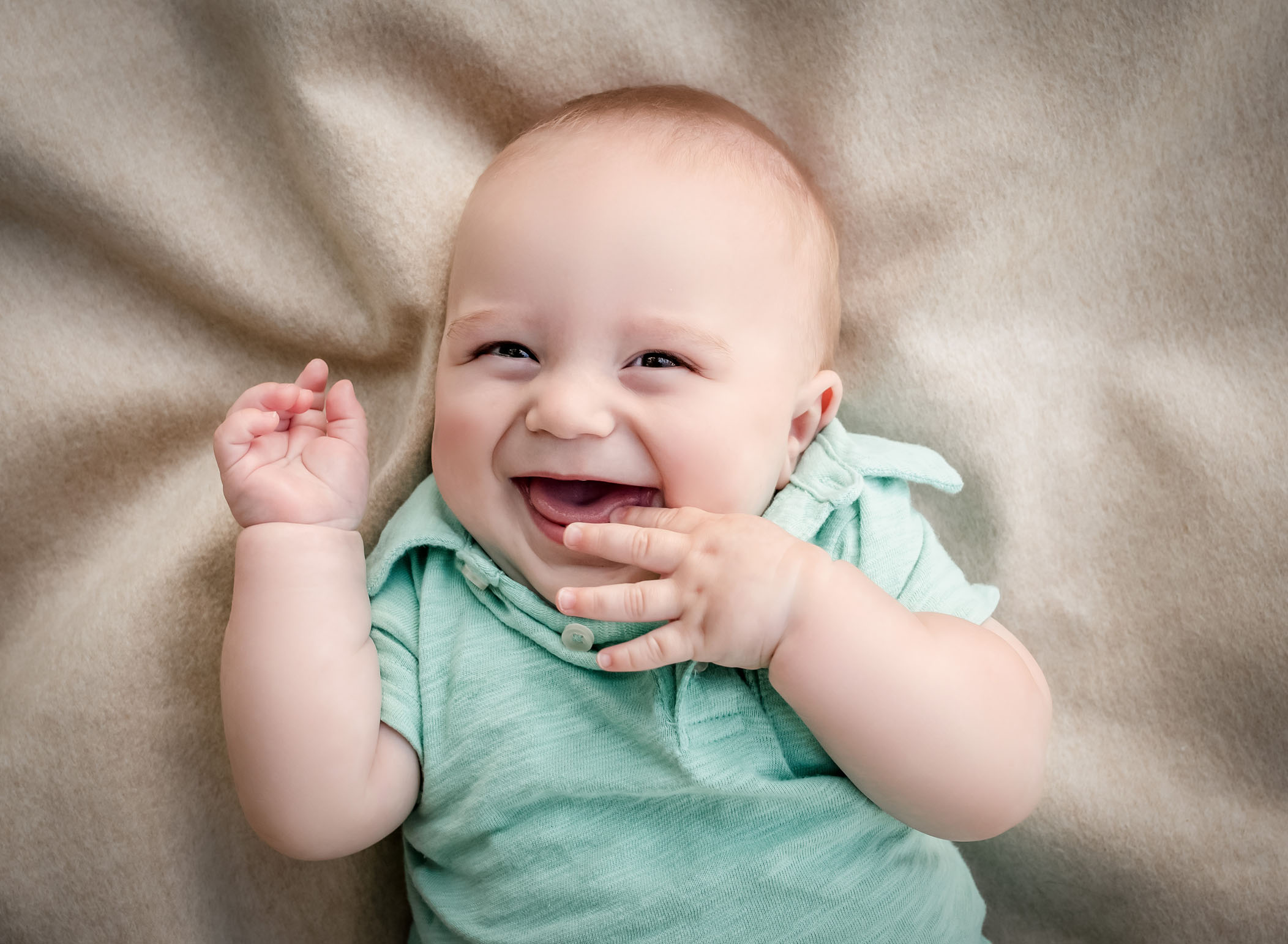 6 month old baby boy laughing with his fingers in his mouth