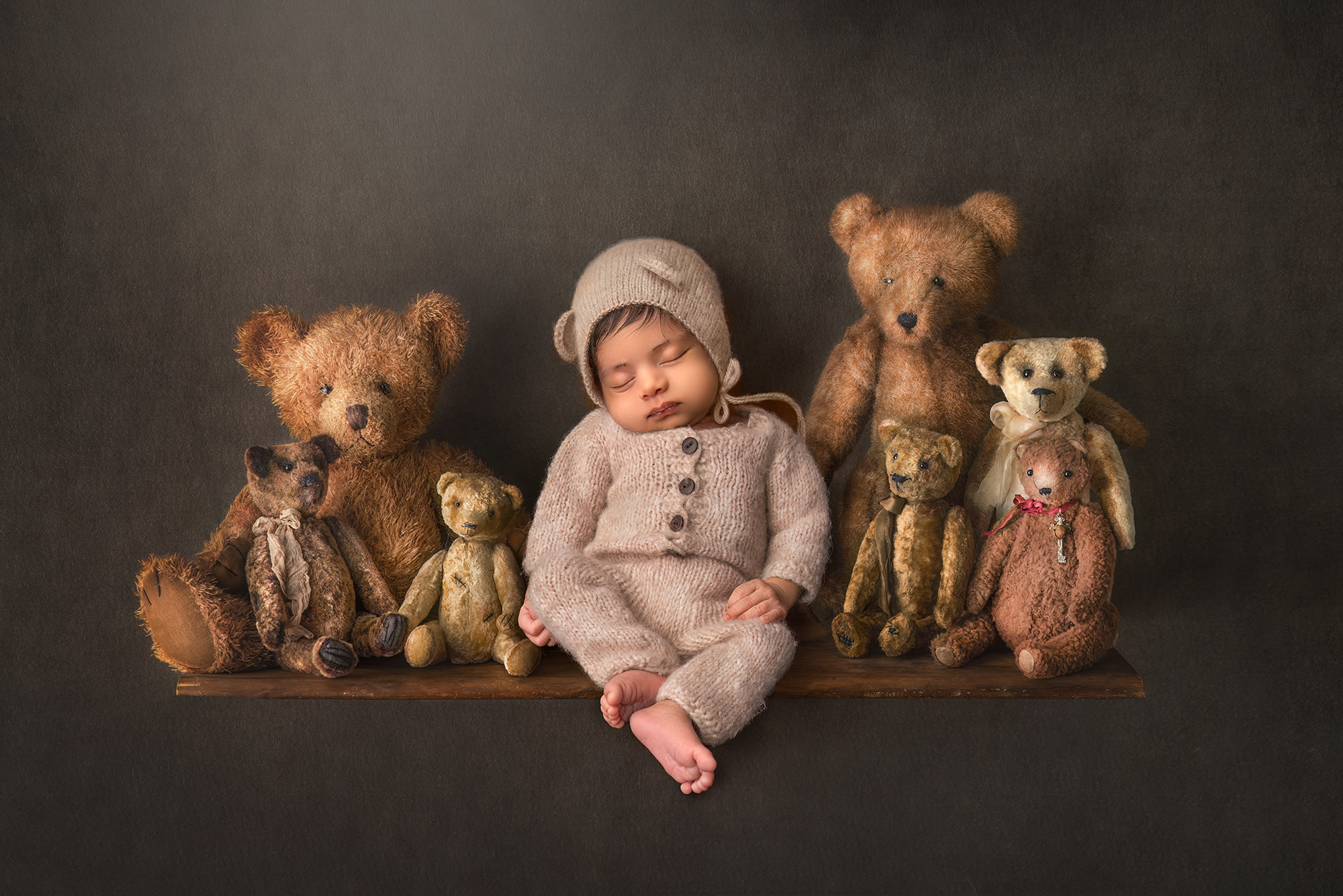 newborn baby boy dressed as a teddy bear asleep on a shelf surrounded by other antique teddy bears Fine Art Newborn Photography