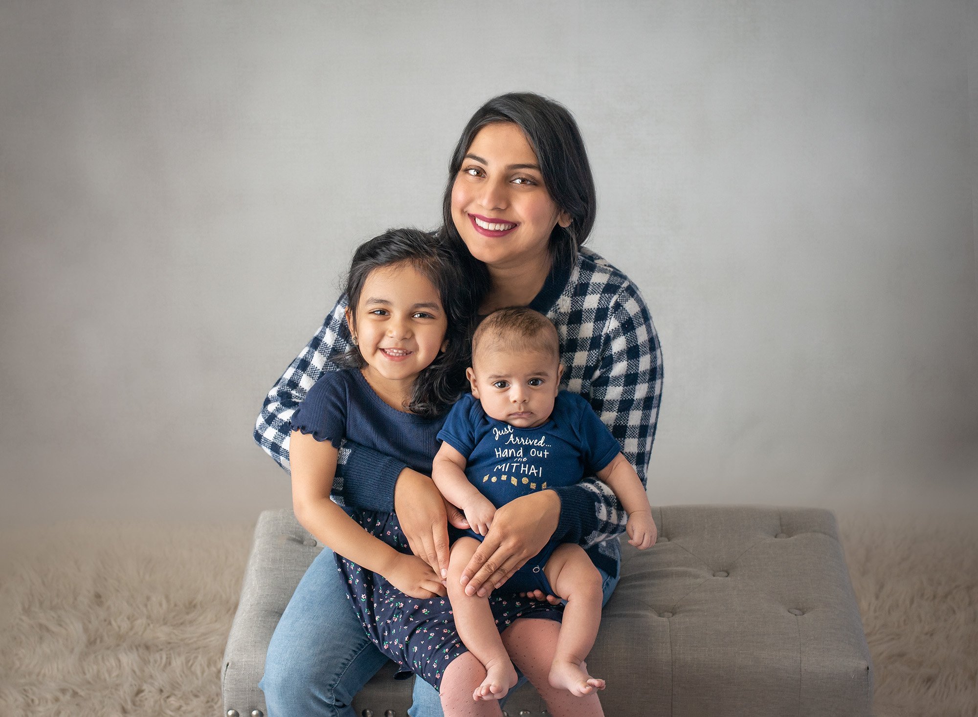 mom smiling holding young daughter and newborn baby boy all dressed in navy blue
