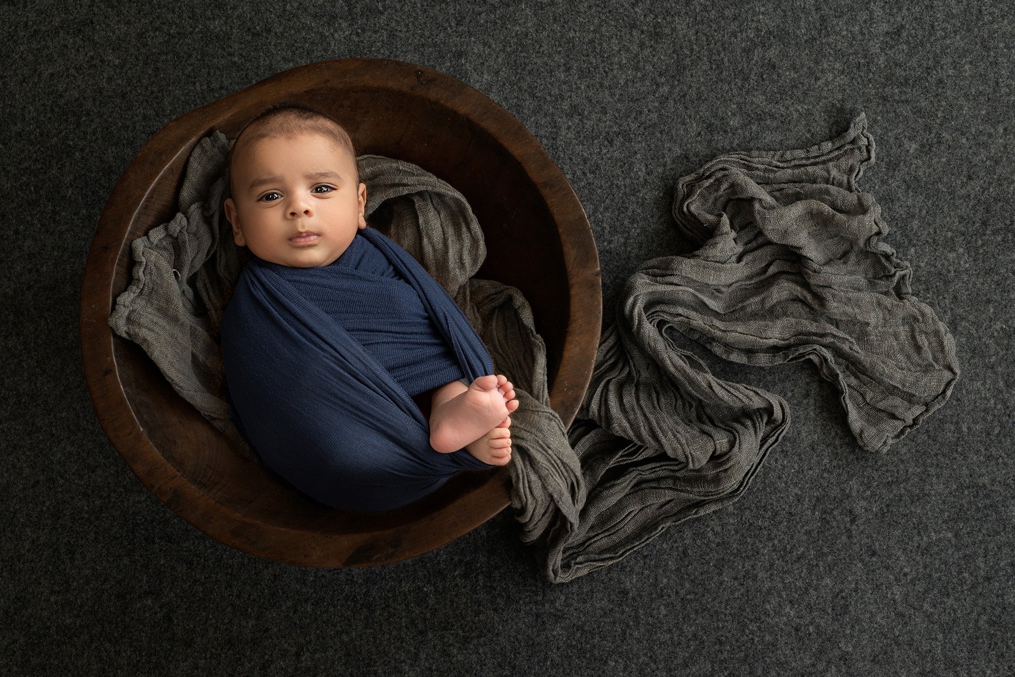 baby portraits newborn baby boy swaddled in blue laying on grey wrap inside wooden bowl