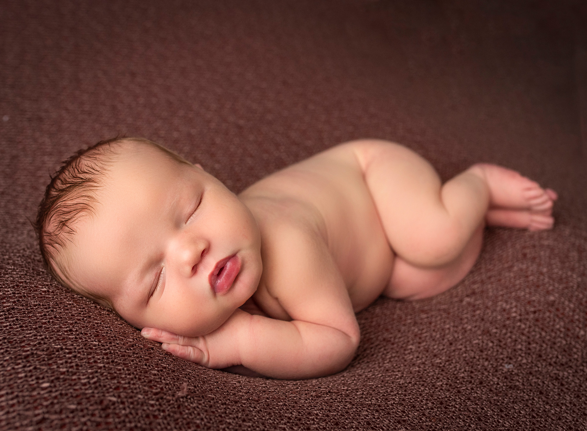 asleep naked newborn baby boy laying on his side on brown blanket