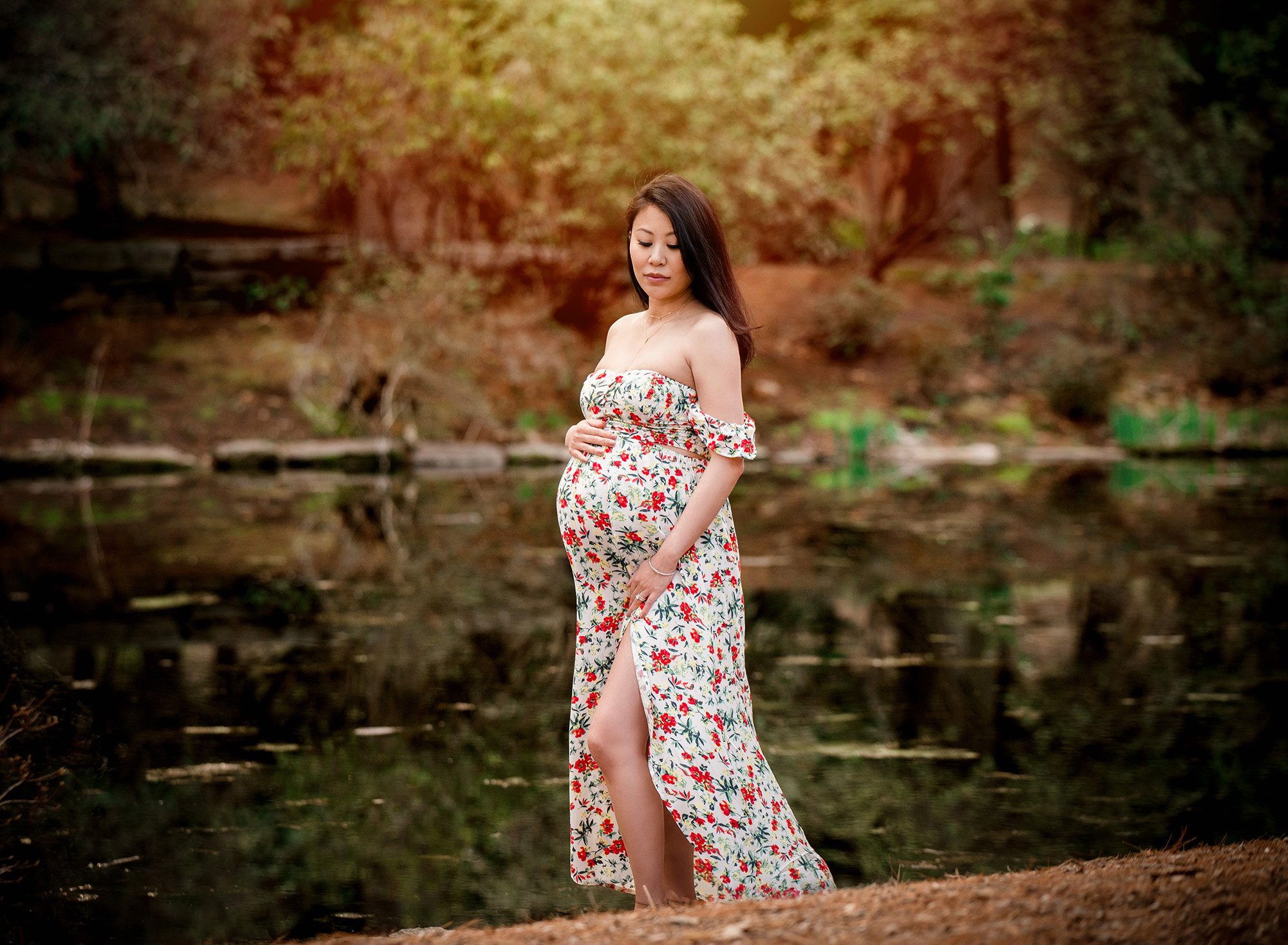pregnant woman in floral maternity dress posing in front of a pond