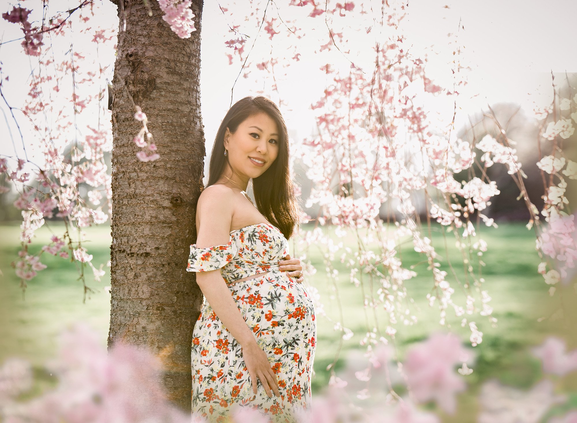garden flower maternity photos pregnant woman in floral maternity dress standing under a weeping cherry tree