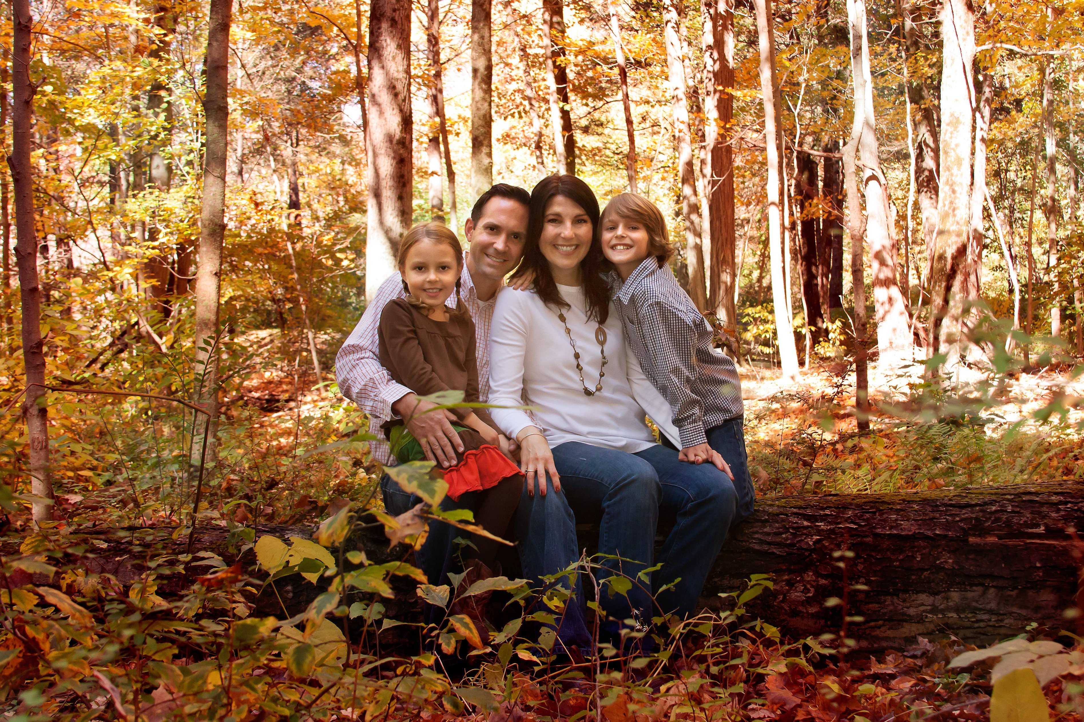 family of four in the woods on a log in the fall