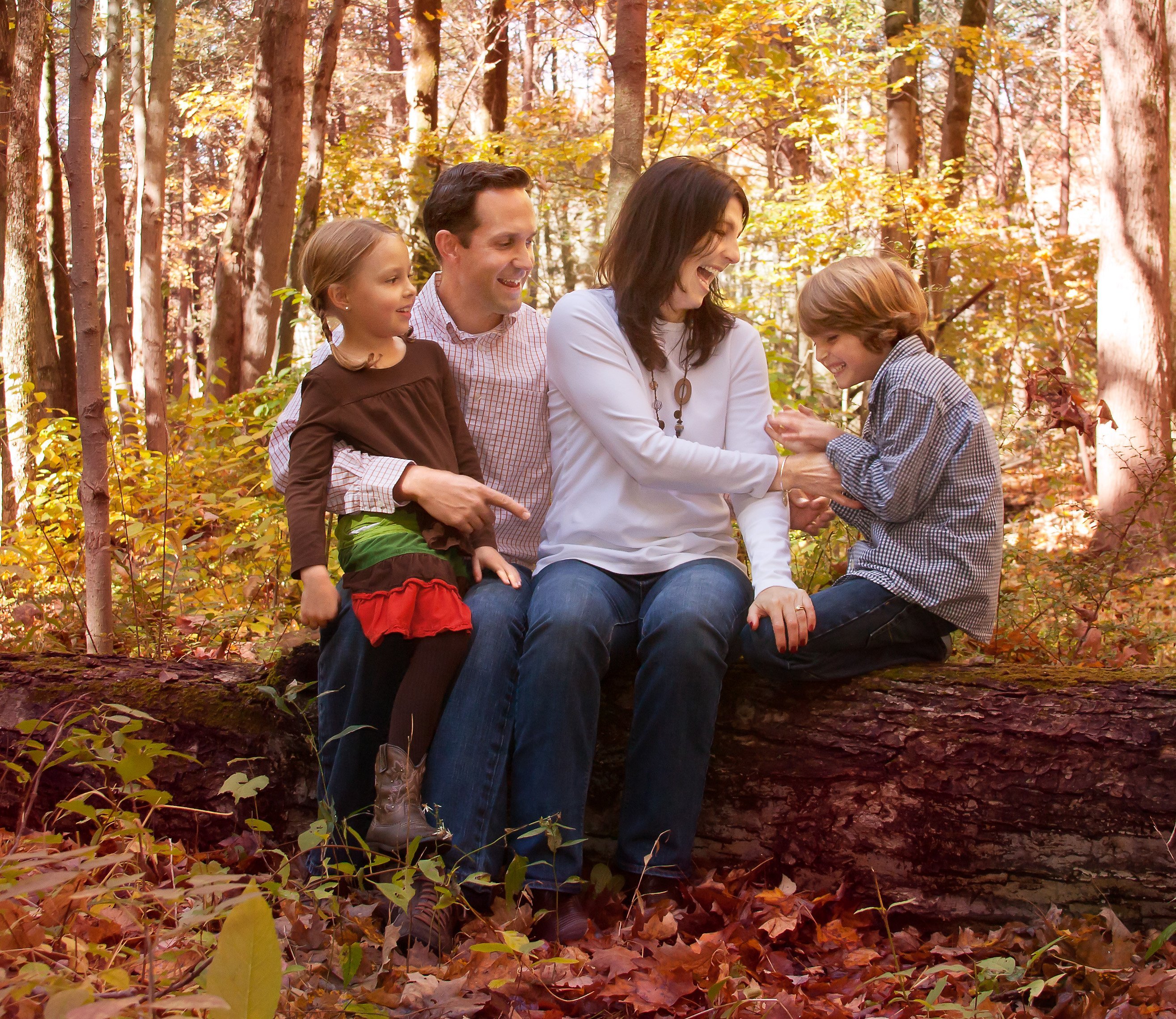 family of four in the woods on a log in the fall laughing