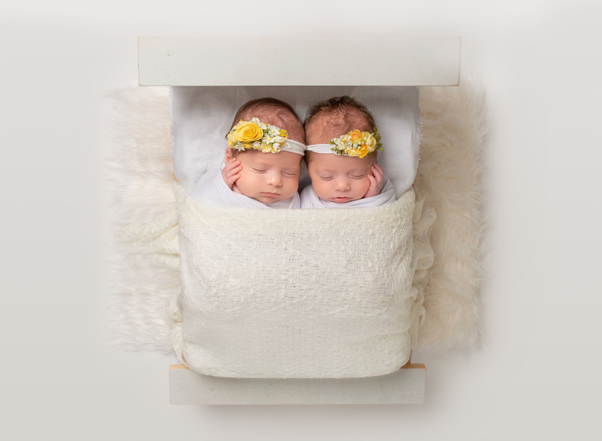 twin newborn baby girls asleep in tiny bed together with yellow floral headbands