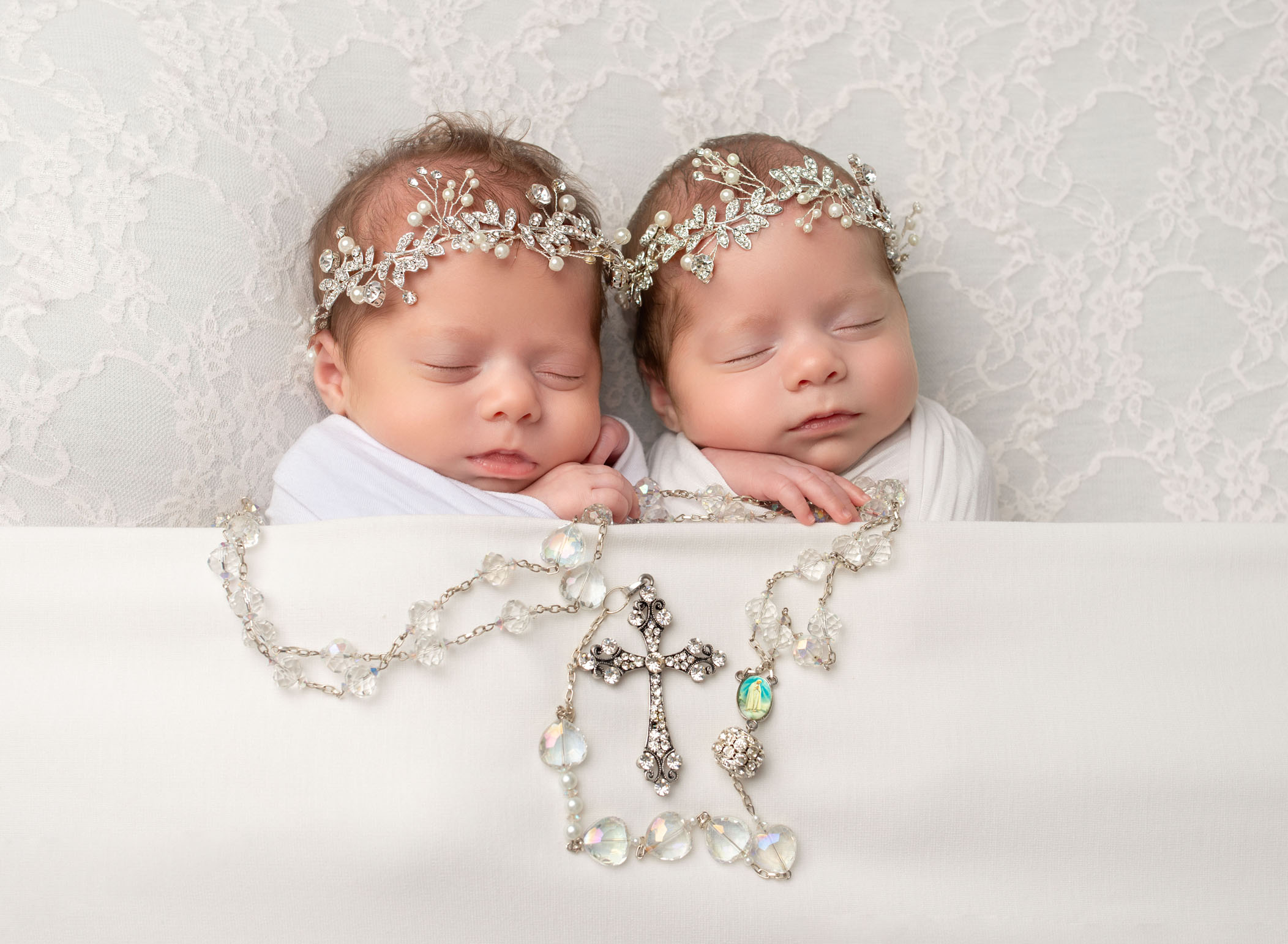 identical twin girls sleeping in bed while holding a large rosary