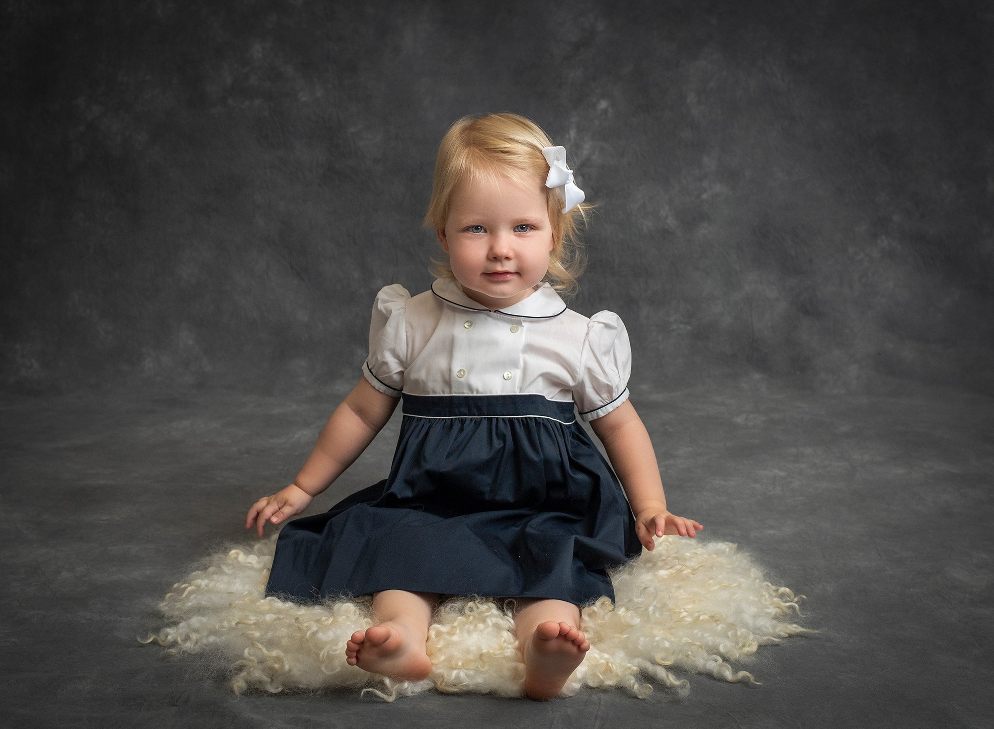 blonde haired little girl sitting on fluffy carpet in vintage dress
