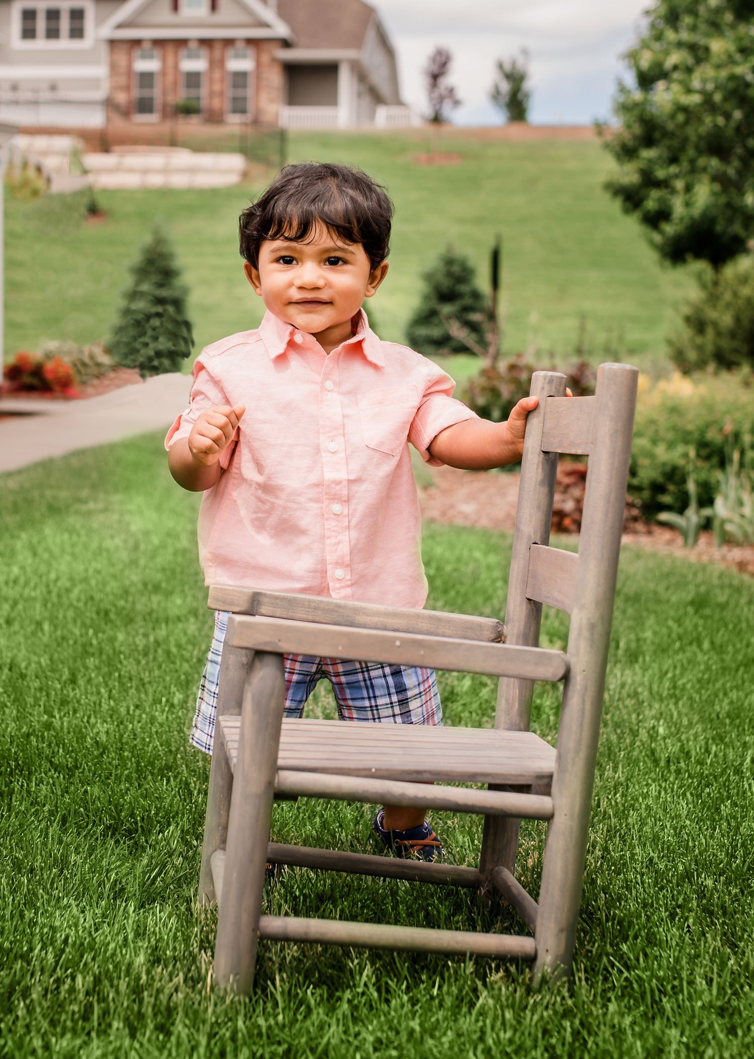 8 mo old boy standing by chair in garden