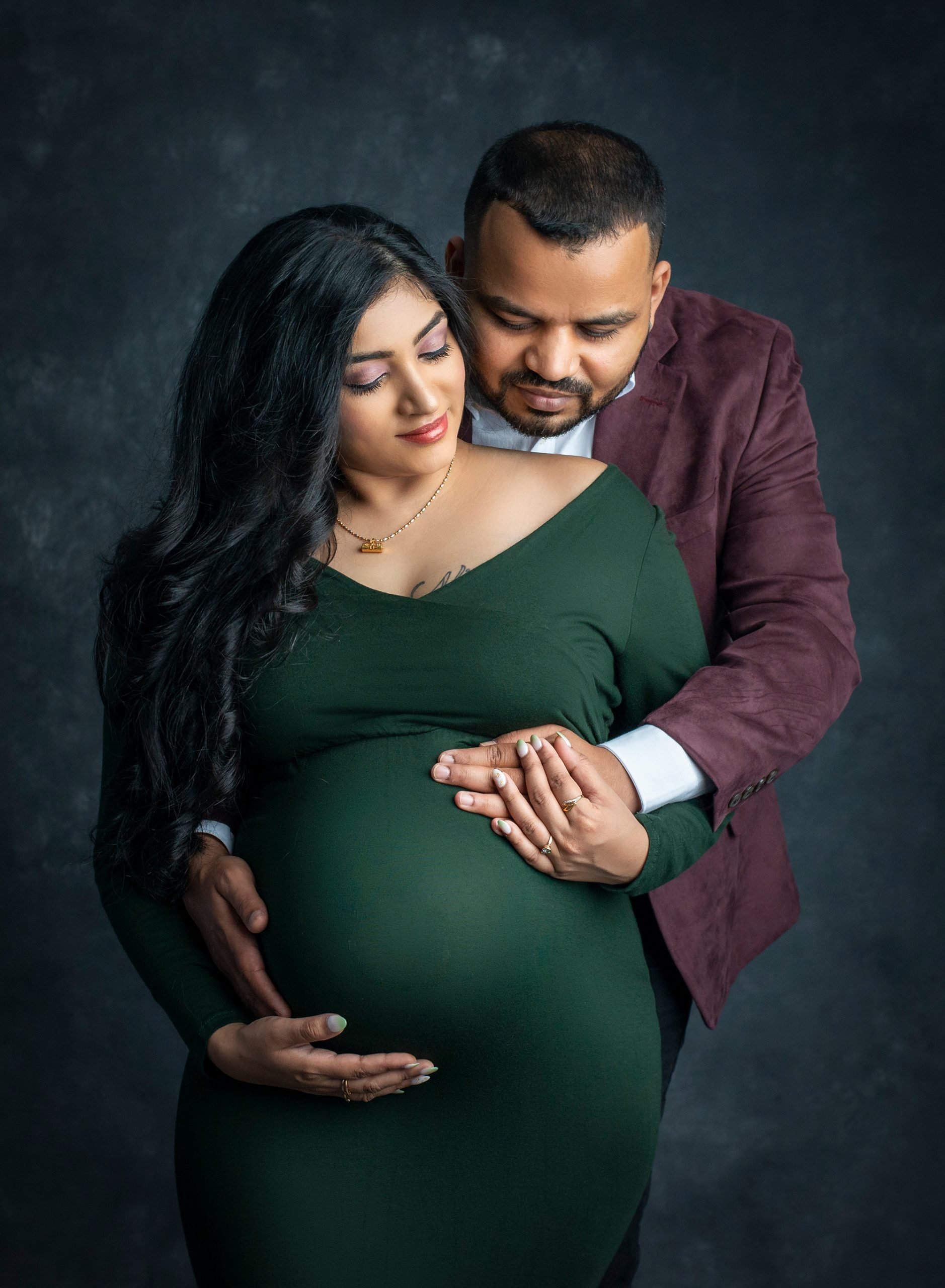 pregnant woman in green dress holding stomach posing with partner