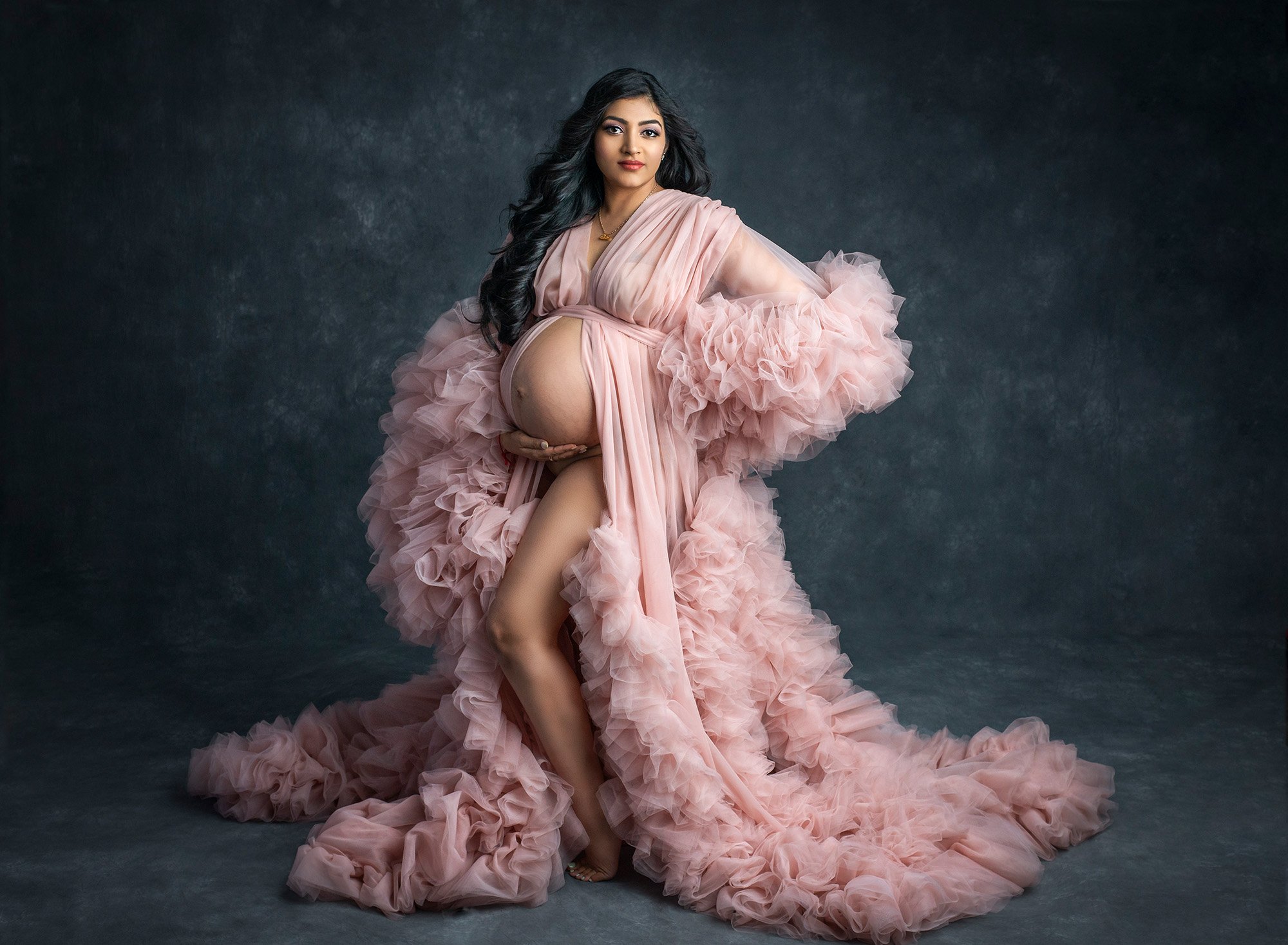 Indian Goddess Maternity photographs pregnant woman posing wearing ruffled pink dress exposing pregnant stomach
