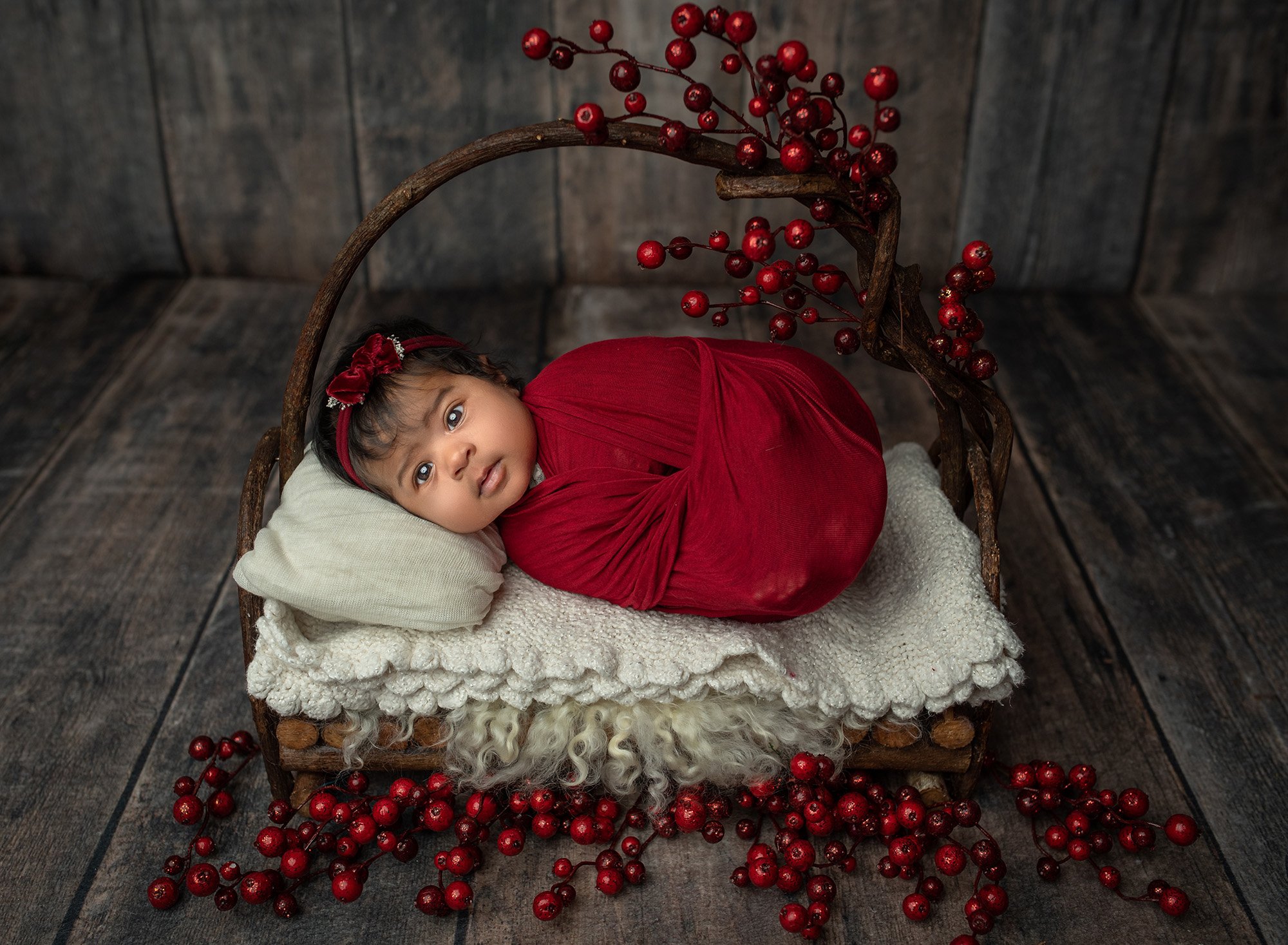 what is the best time for a newborn photoshoot 6 week old baby girl swaddled in red lying on a rustic wood bed with red winter berries around her best time to take newborn photos