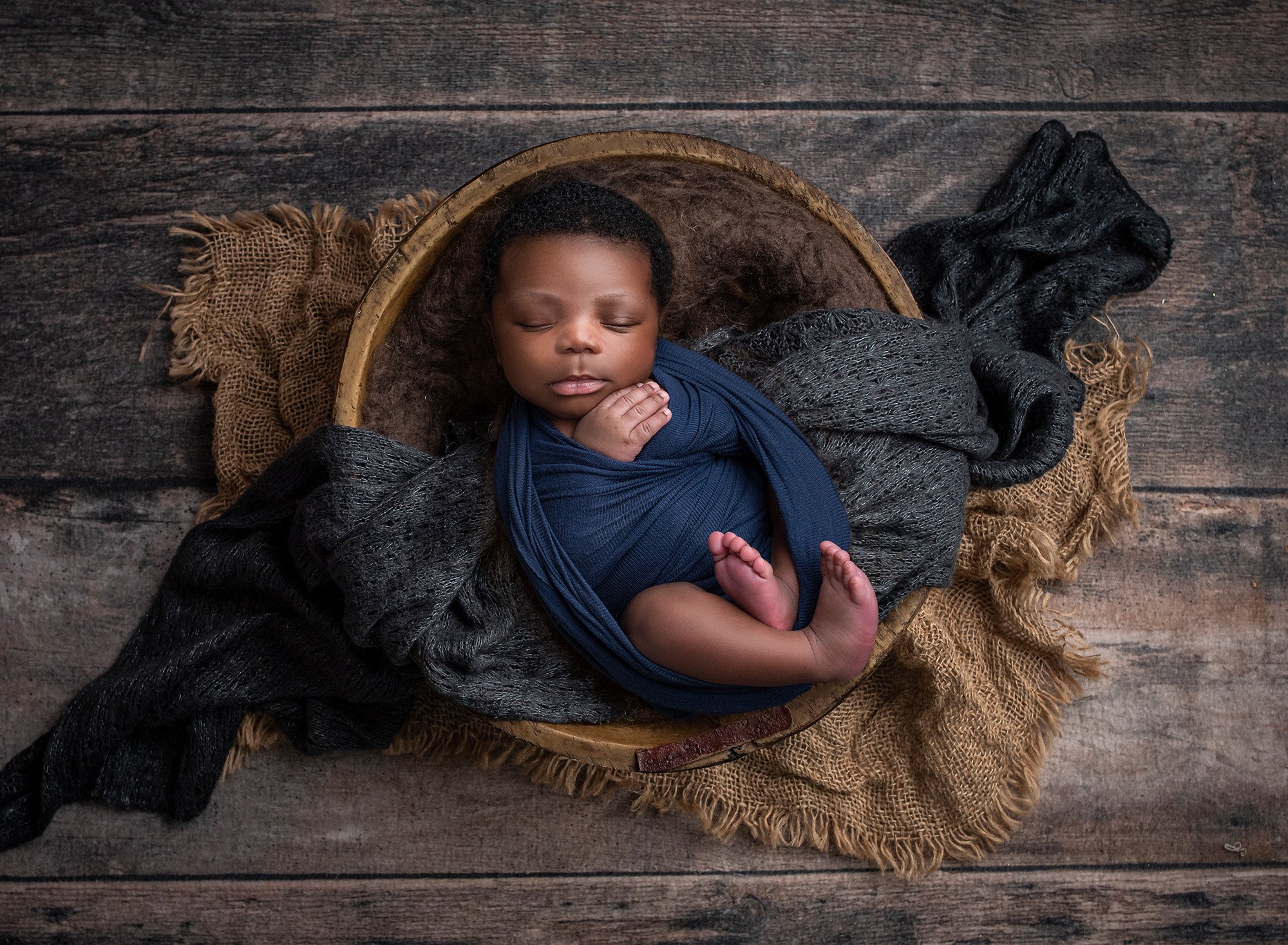 newborn baby boy swaddled in navy asleep in wooden bowl