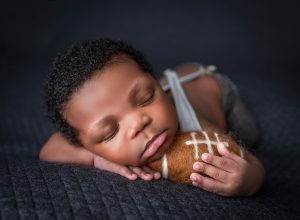 newborn baby boy asleep holding felt football
