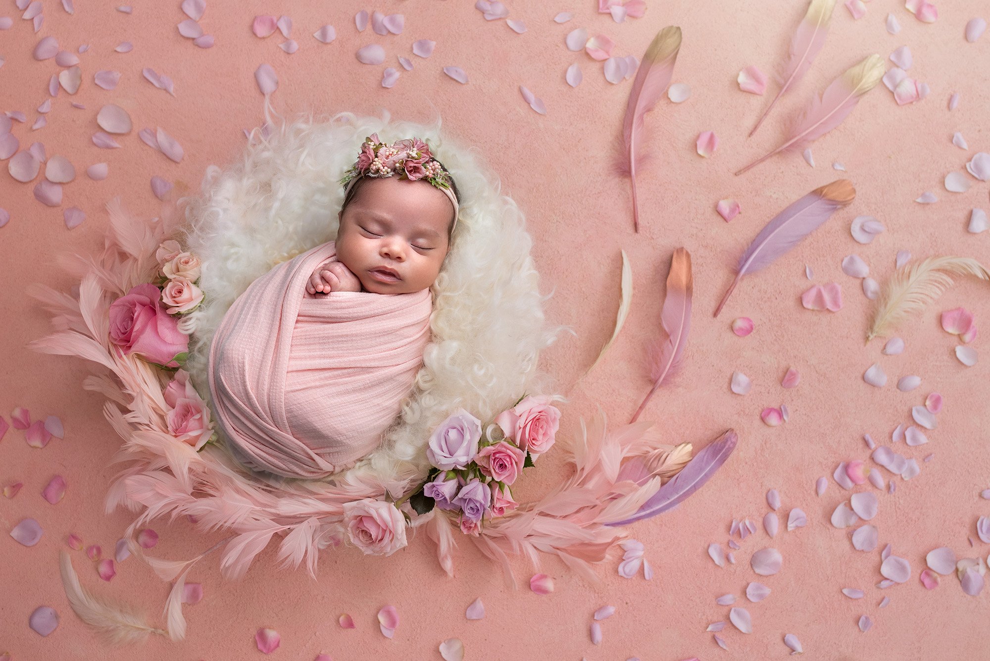 girly girl newborn photos newborn baby girl swaddled in pink sleeping on fuzzy blanket surrounded by feathers and flower petals