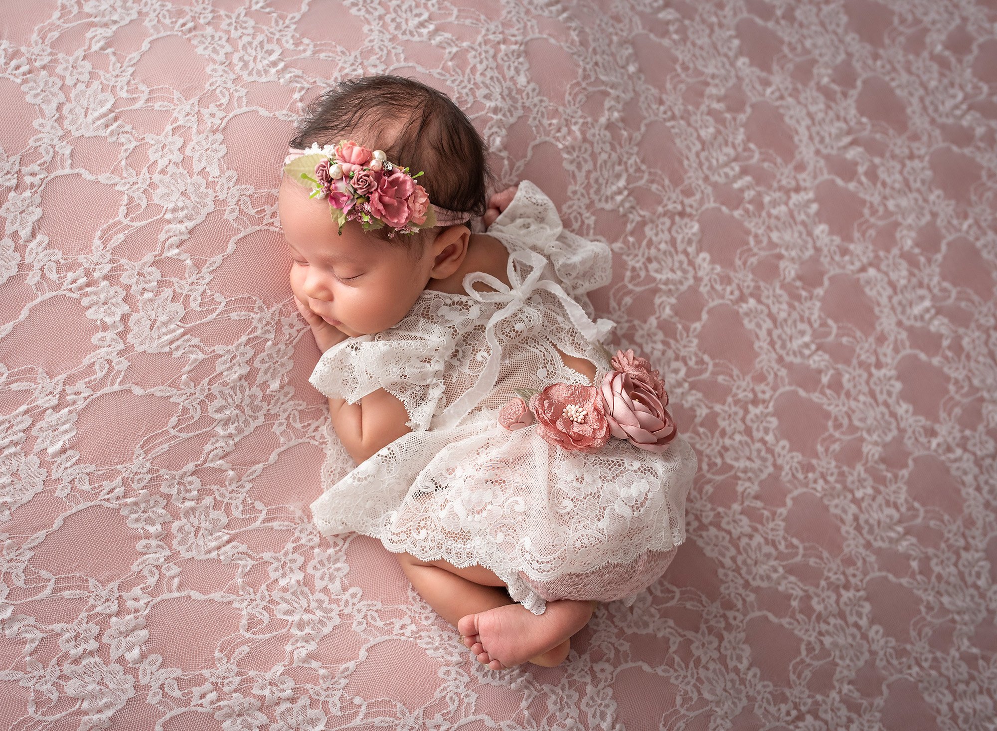 girly girl newborn photos newborn baby girl laying on stomach on top of pink lace wearing lace dress and pink floral headband