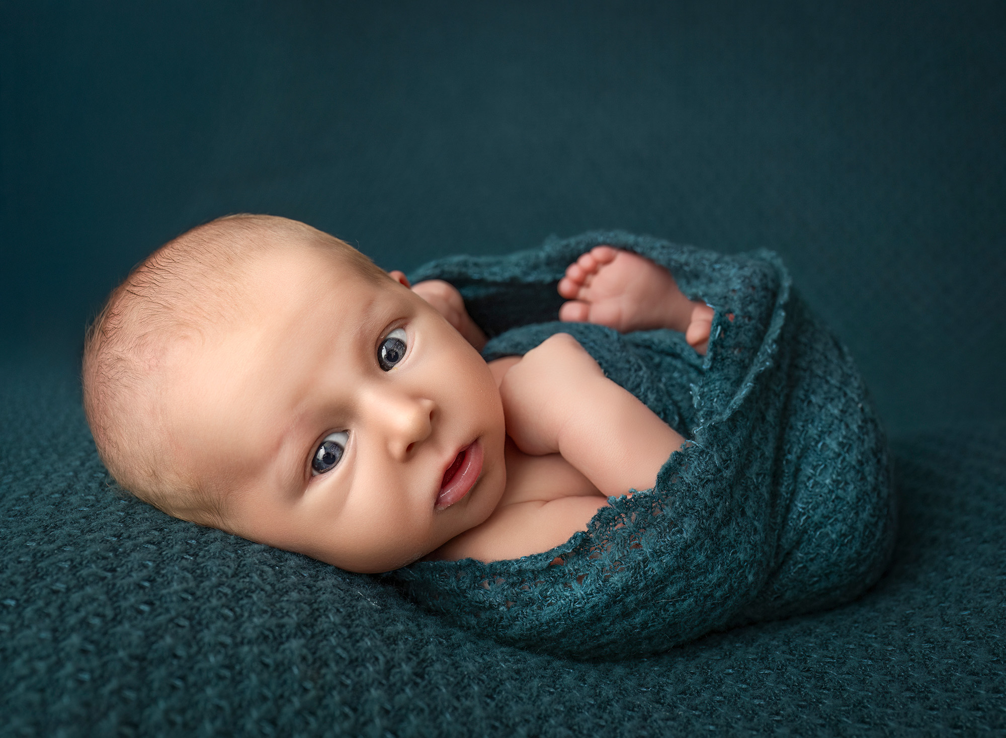 Levi awake and bundled in teal knit, tiny toes peeking out on matching fabric.