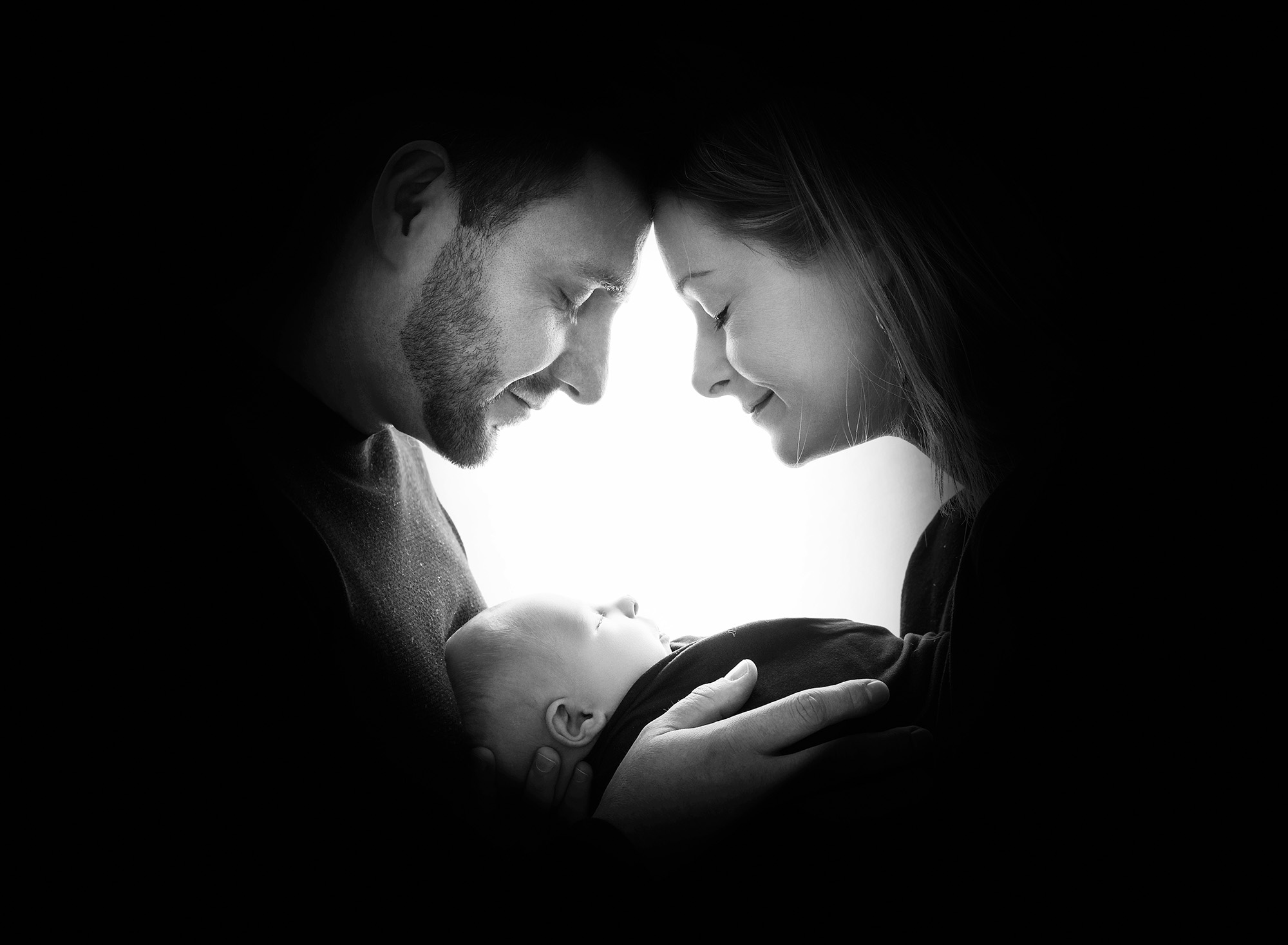 Black-and-white family portrait with parents forehead-to-forehead, cradling Levi.