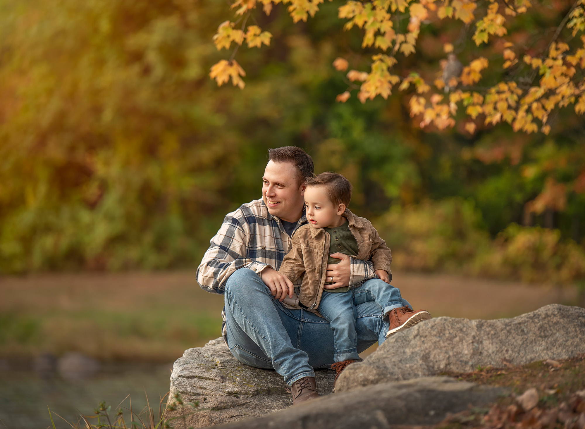 Dad and Lincoln sitting on a rock under warm fall branches.