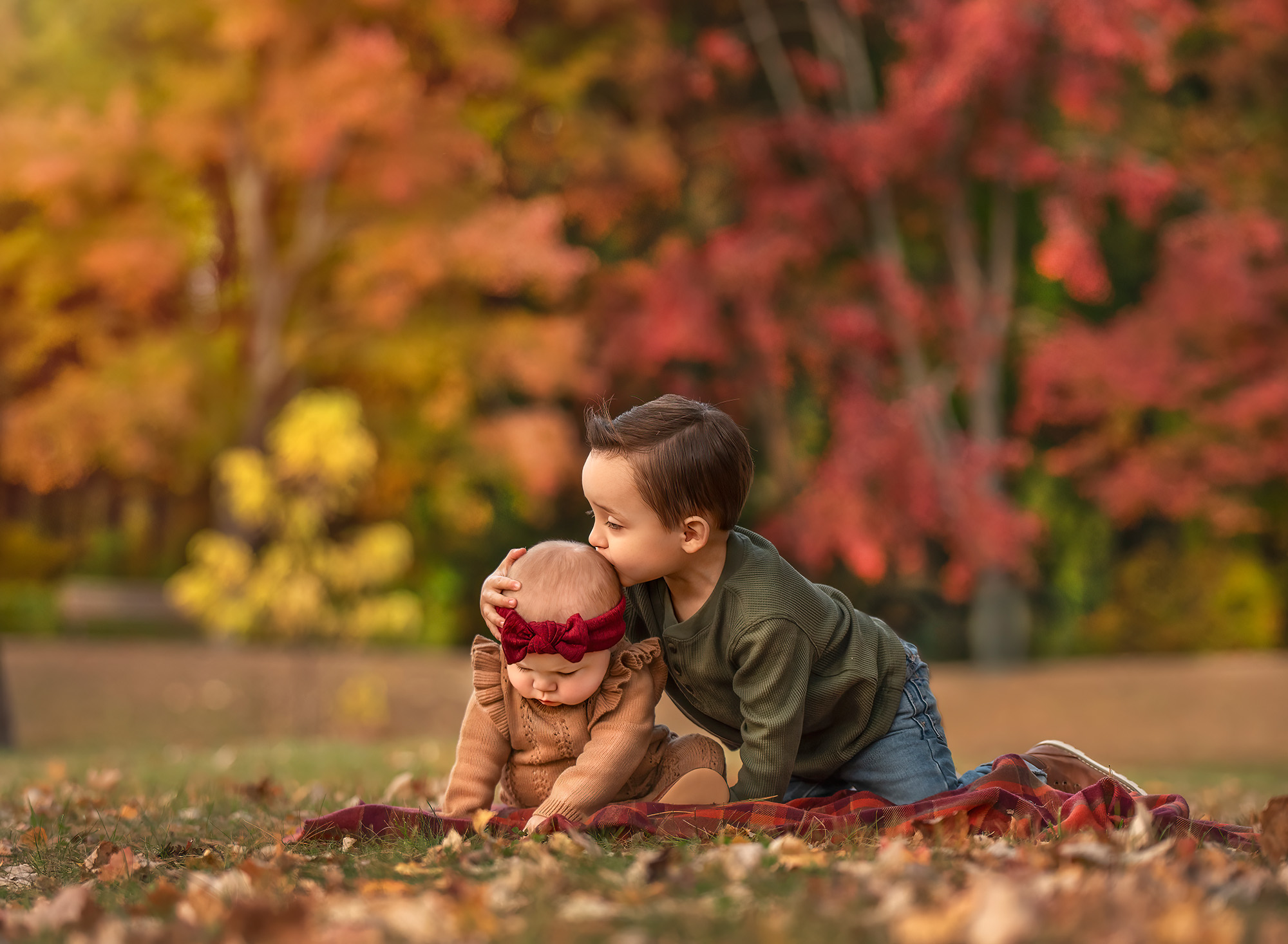 Lincoln kissing Kennedy’s head while they play on a leaf-covered lawn.