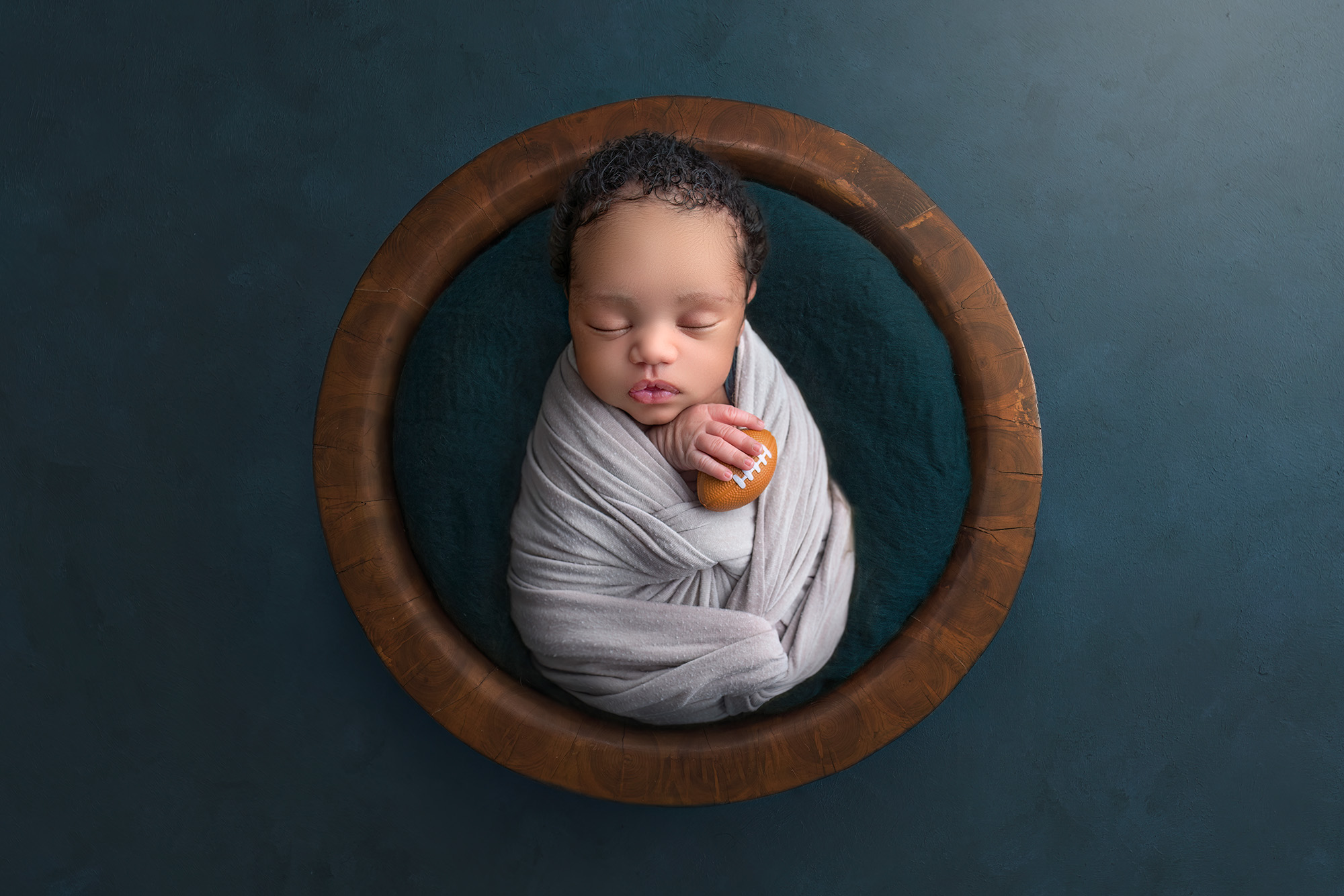 Maternity and Newborn Photographer Newborn boy asleep in a wooden bowl holding a tiny football