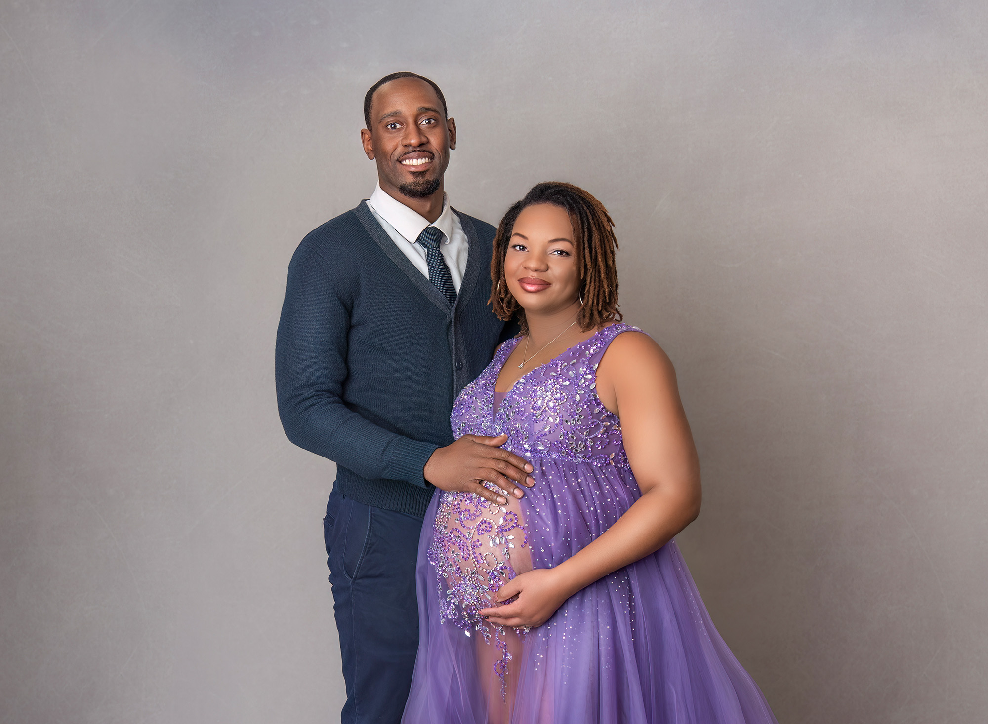 Pregnant woman wearing a purple sparkly gown posing with spouse