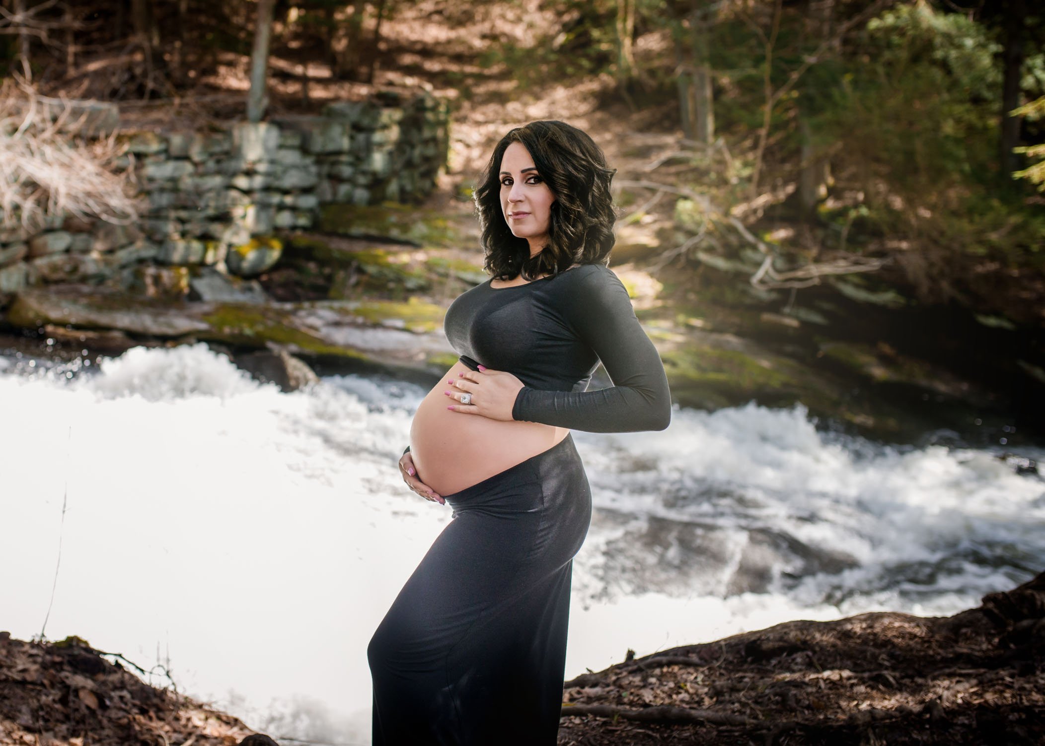 pregnant woman poses in front of white water in the forest