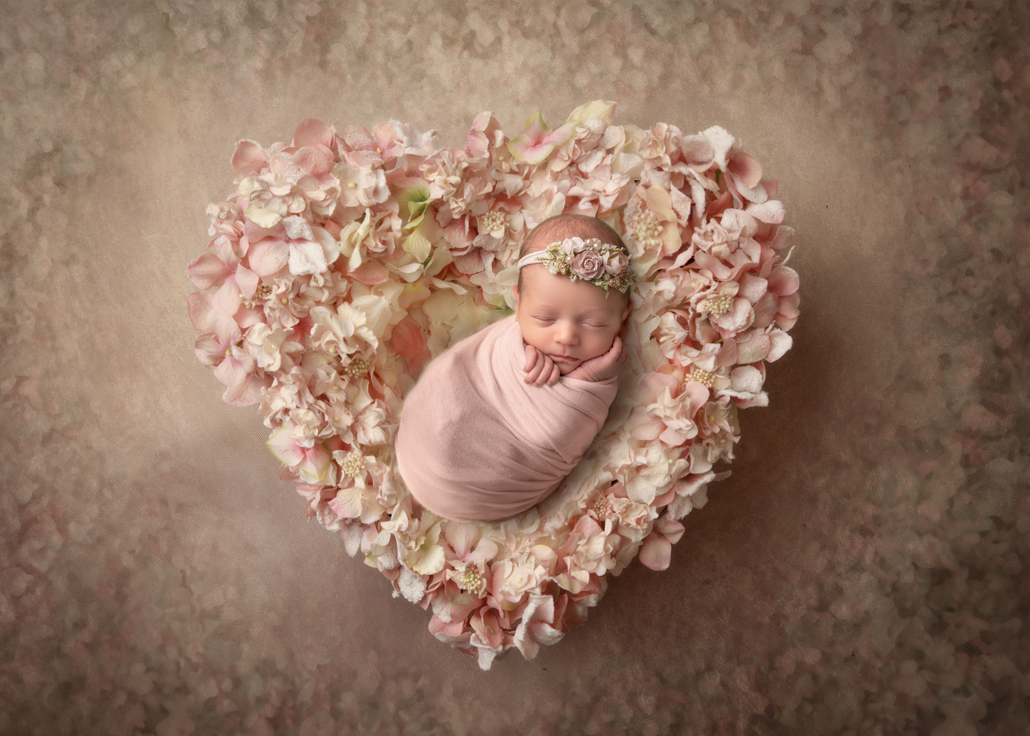 swaddled newborn girl sleeping in a heart shaped basket covered in rose petals