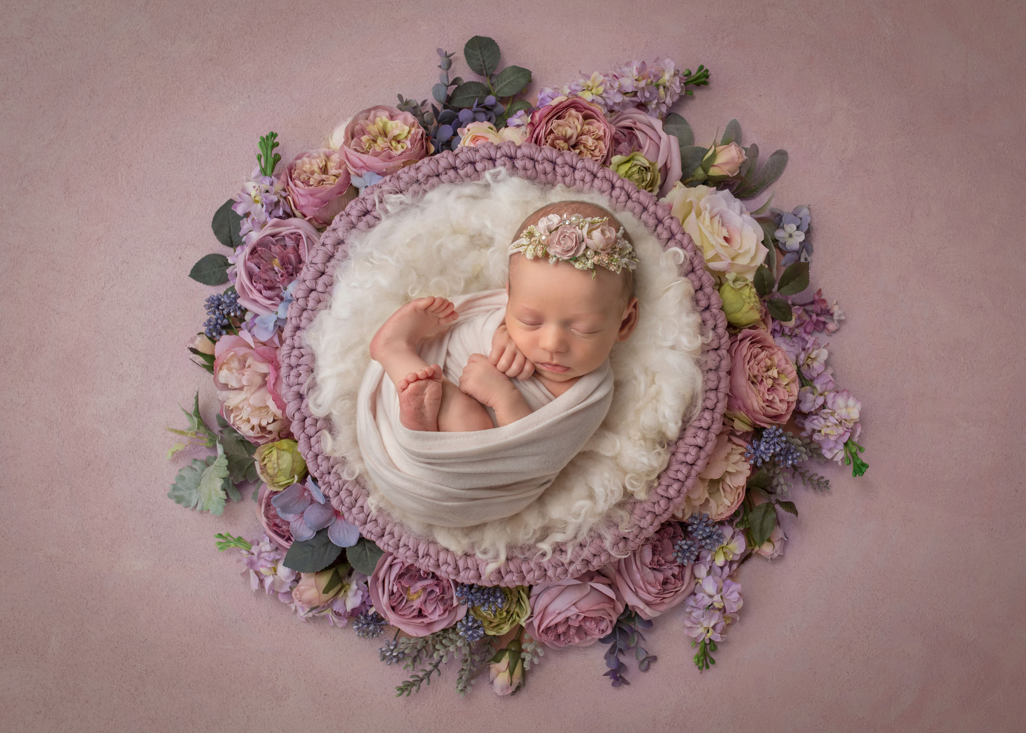newborn baby girl swaddled and sleeping in a circle of lilac colored flowers