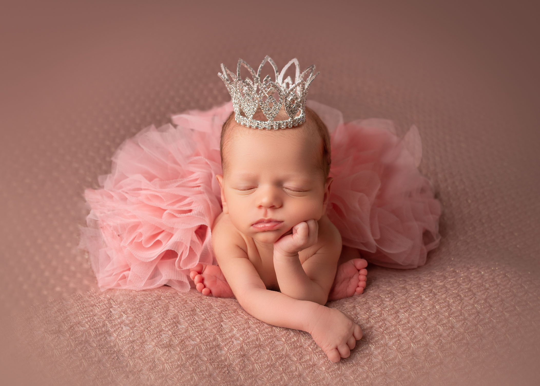 newborn baby girl sleeping in modified froggy pose with a crown on her head
