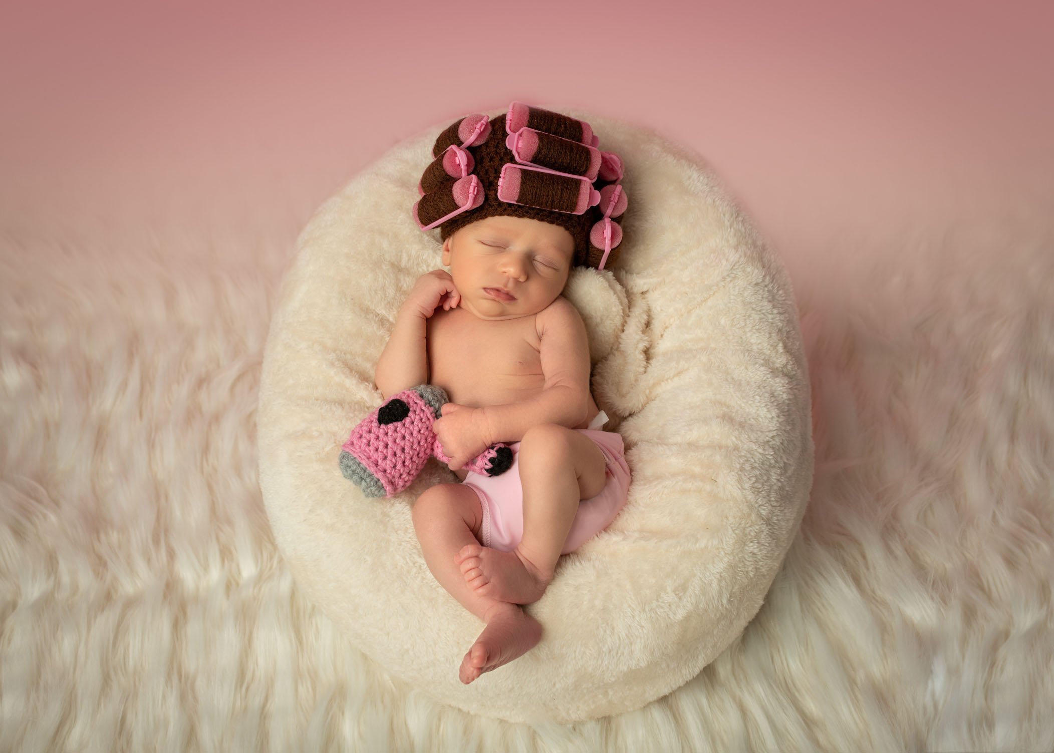 newborn baby girl wearing hair curlers and holding a crocheted hair dryer