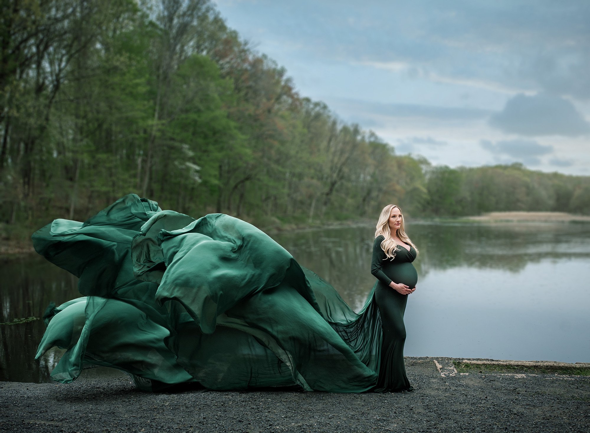 Connecticut Maternity Photographer Beautiful blonde woman wearing a gorgeous flowing emerald green gown I’m front of a lake on a stormy day