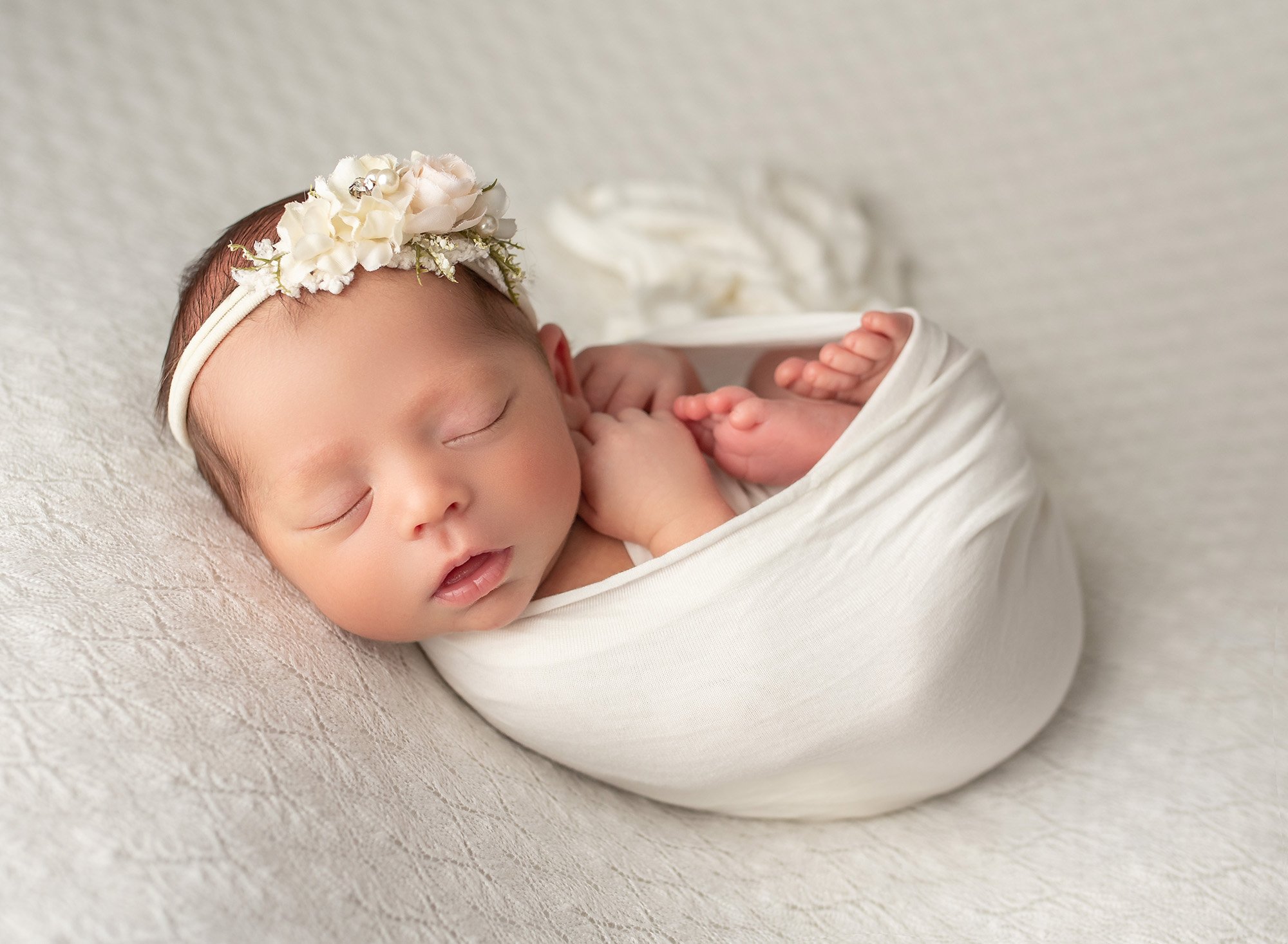Light and Feminine Newborn Photos baby girl wrapped in cream swaddle wearing cream floral headband asleep