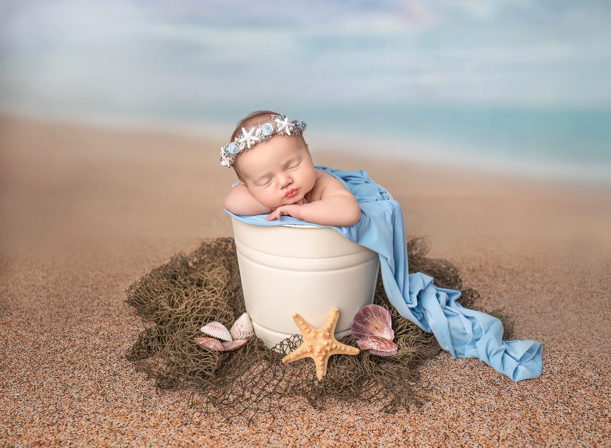 Connecticut newborn photographer Beach-themed newborn portrait — Newborn in a cream bucket on sand with shells and starfish.