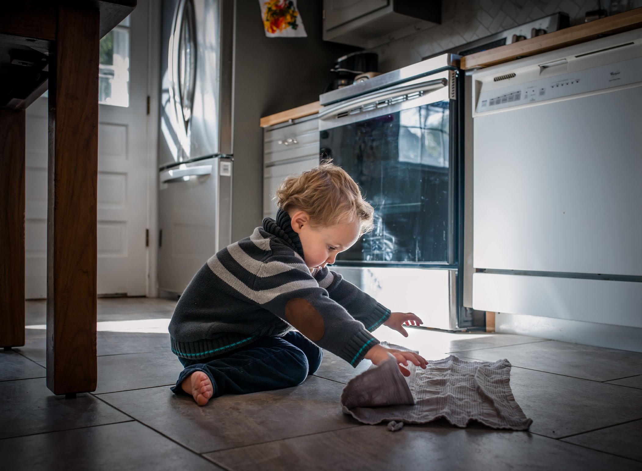 4 year old boy folding a towel on kitchen floor