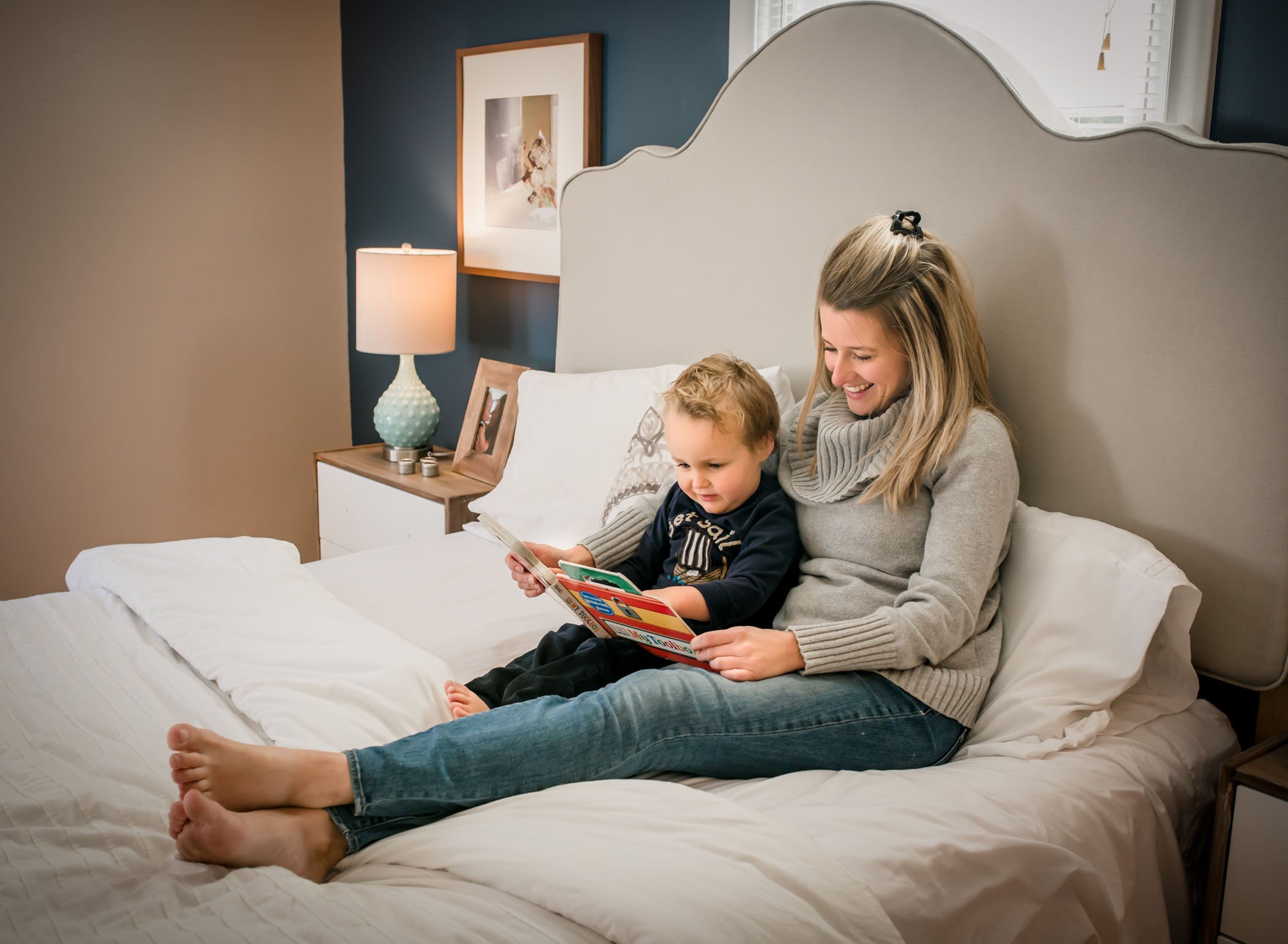 Mom and toddler son reading a book on the bed
