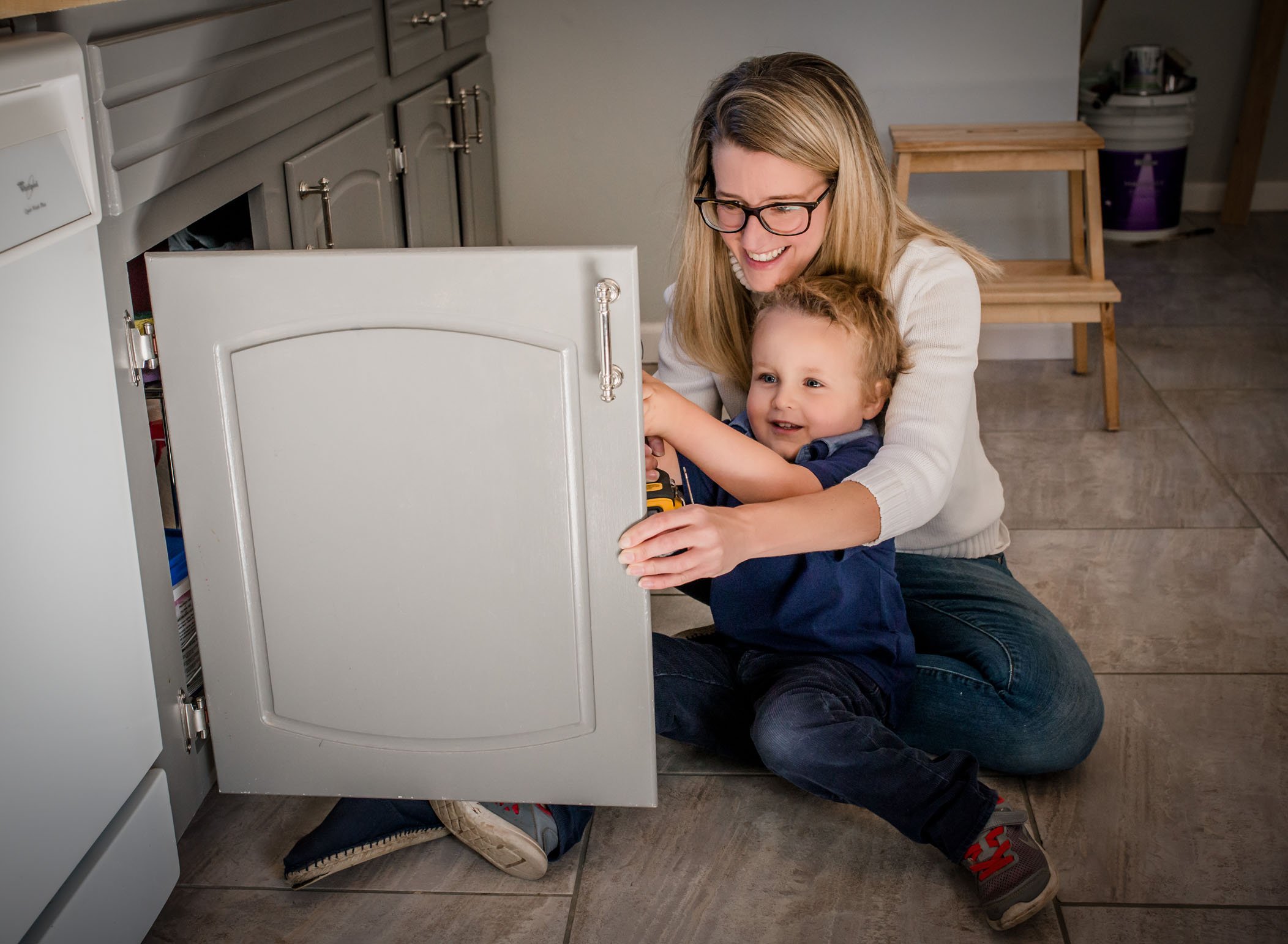 Mom & toddler son fixing cabinet in kitchen