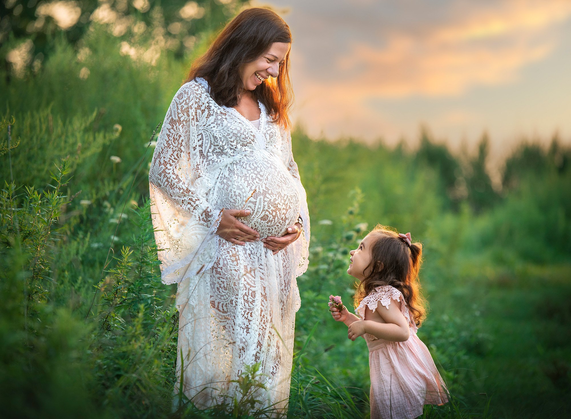 little girl wearing pink dress smiling up at her expecting mother wearing a bohemian laced dress