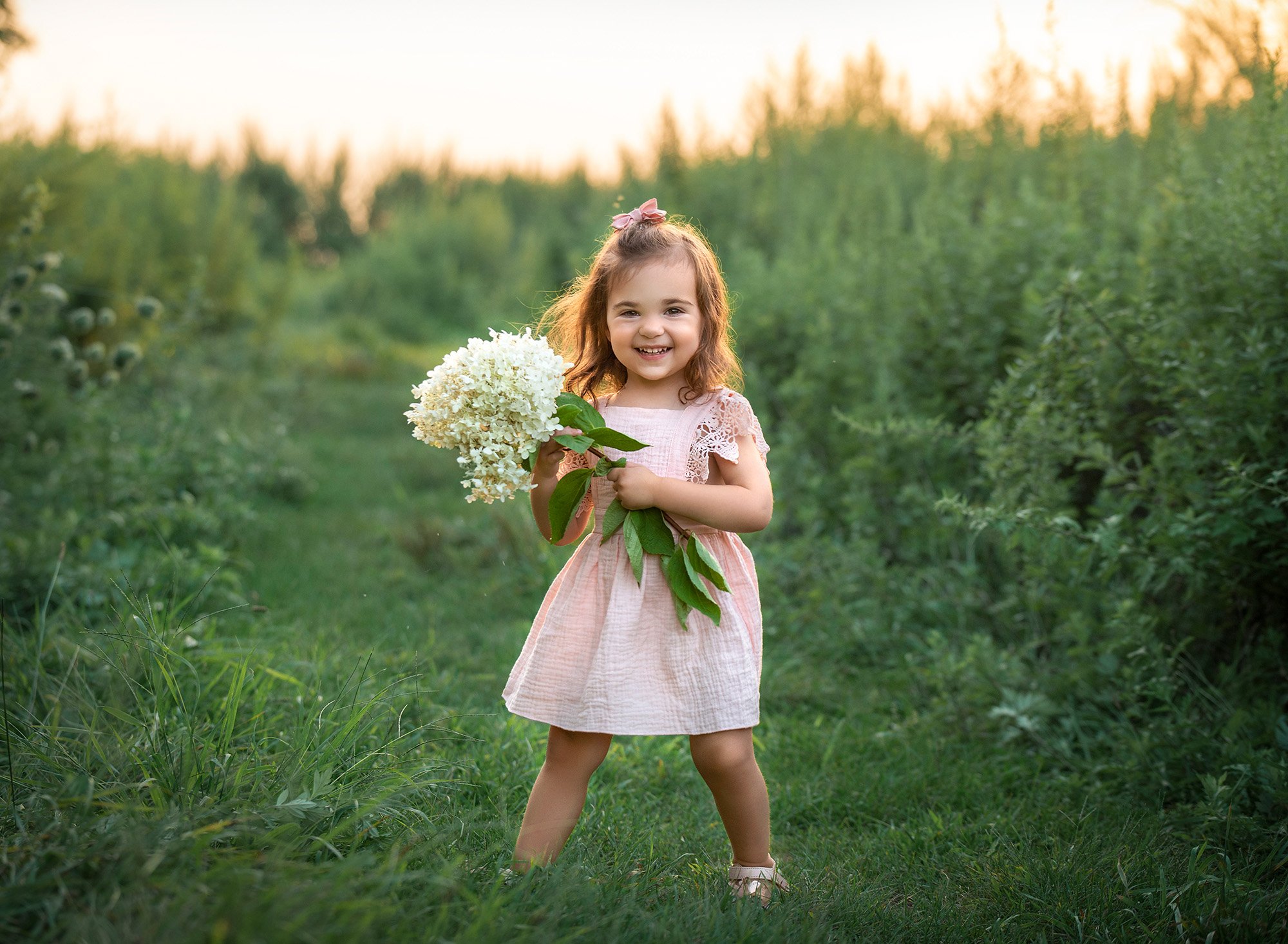 little girl in pink dress smiling in a field while holding white flowers