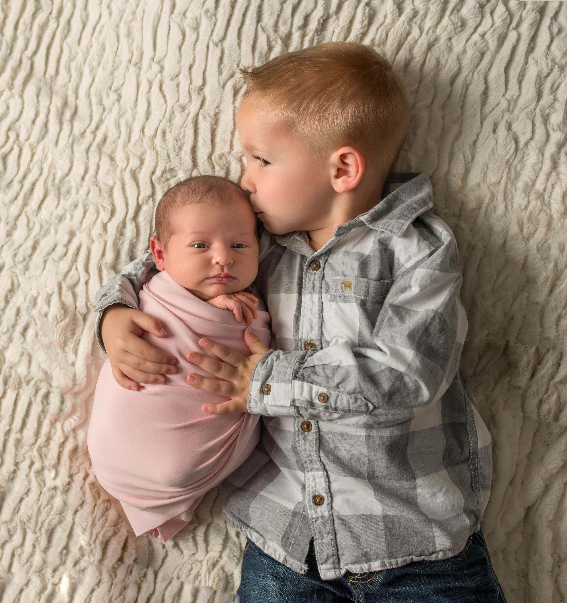 4 year old big brother holding newborn baby sister and kissing her
