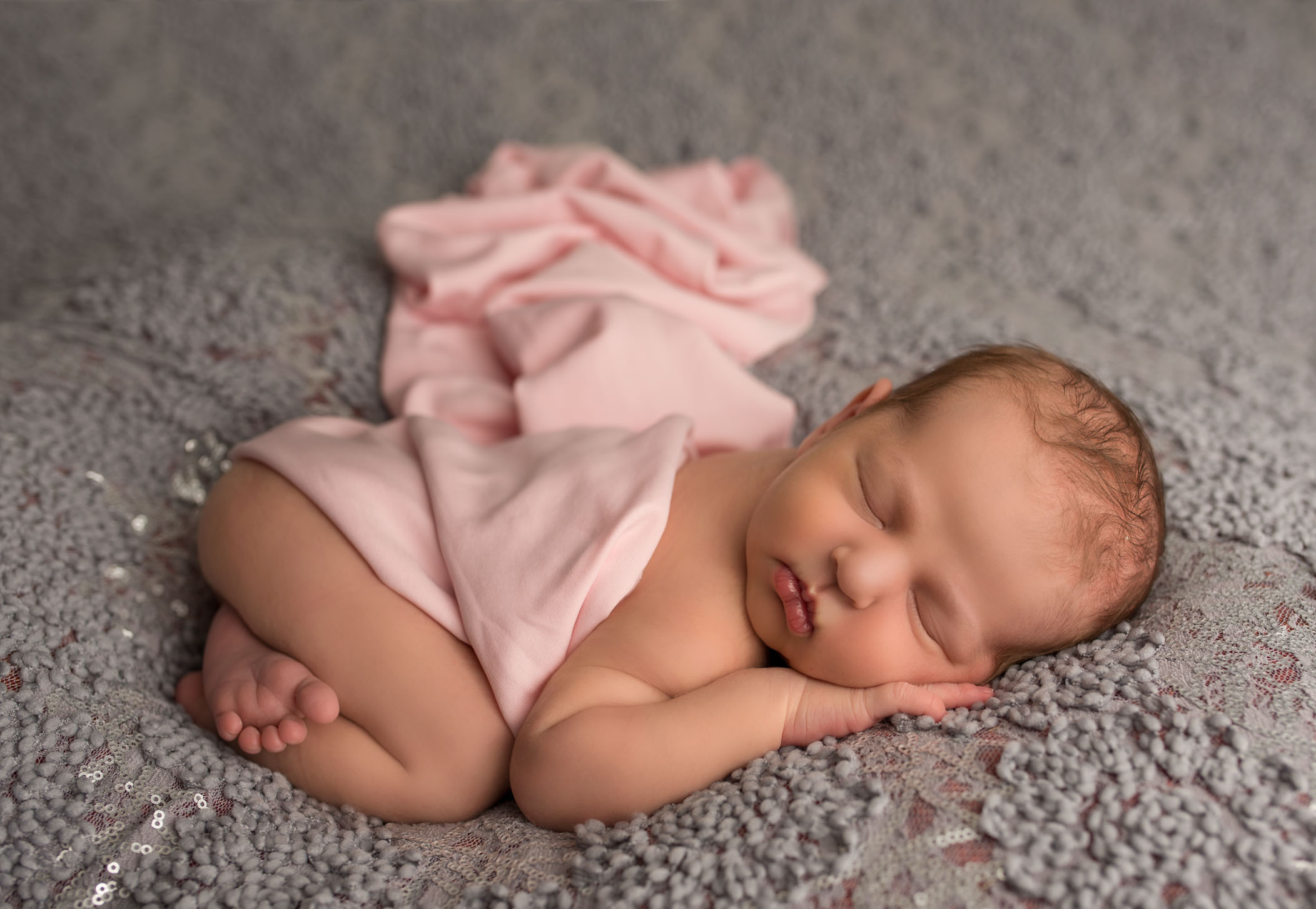 newborn baby girl sleeping on fancy grey background with pink wrap