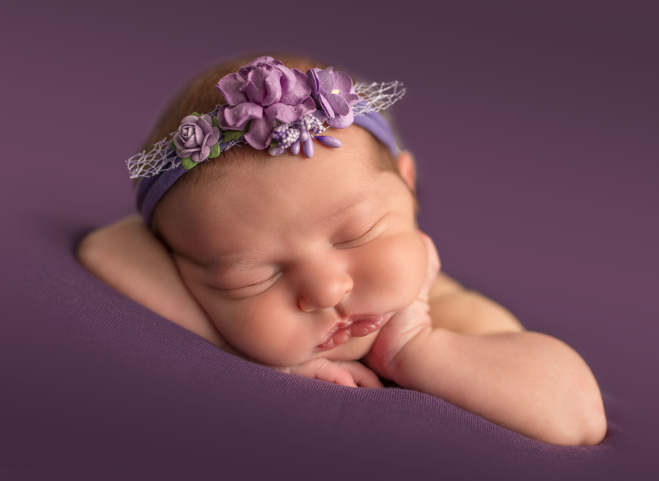 newborn baby girl sleeping with hand on cheek and purple floral headband