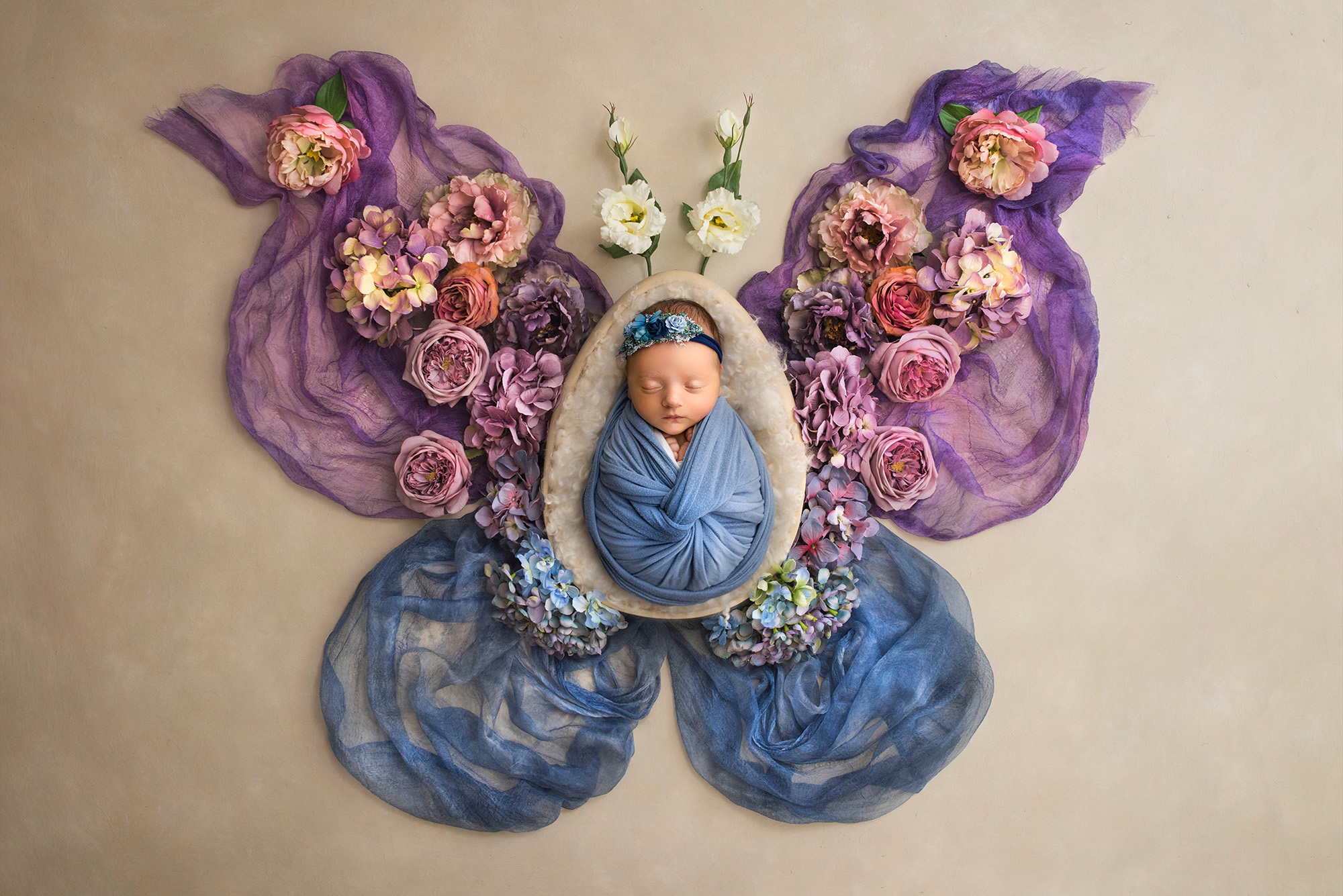In the center of a floral butterfly, a precious newborn wrapped in blue exudes serenity and beauty