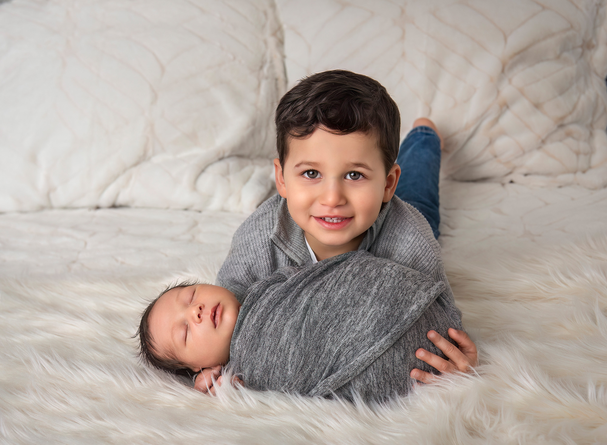 Older brother cradling baby brother fast asleep on bed