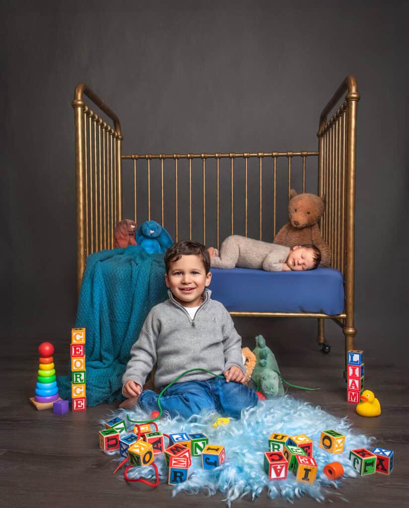 Newborn Family Photography Older brother playing with toys in front of crib newborn brother is sleeping in