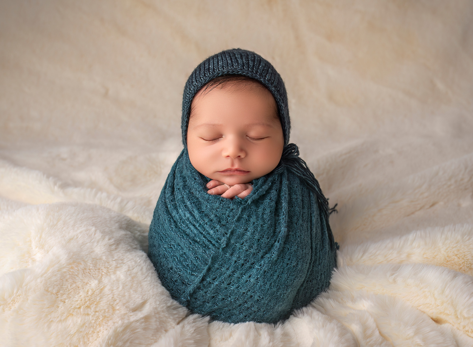 Newborn baby boy posed fast asleep in a teal wrap and bonnet