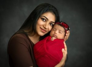 mother cradling newborn baby girl swaddled in red